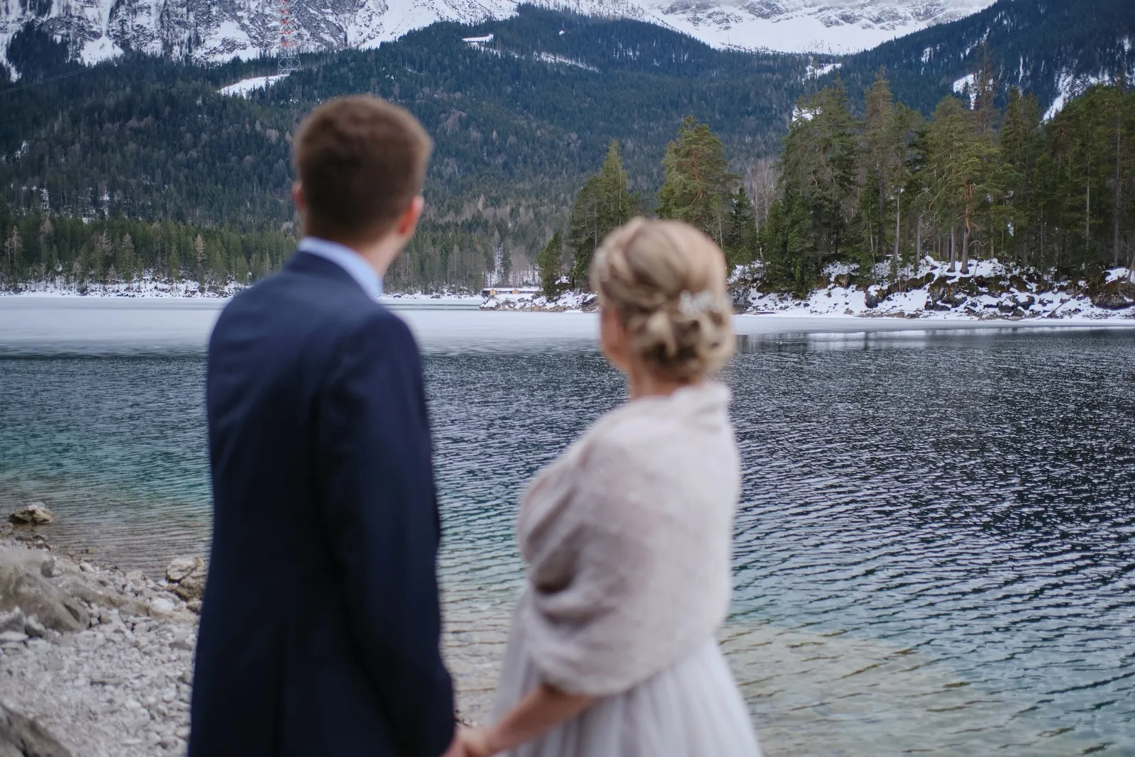 Brautpaar Hand in Hand am Ufer des winterlichen Eibsees, Schnee und Bergpanorama im Hintergrund – After Wedding Christina & Florian, Eibsee