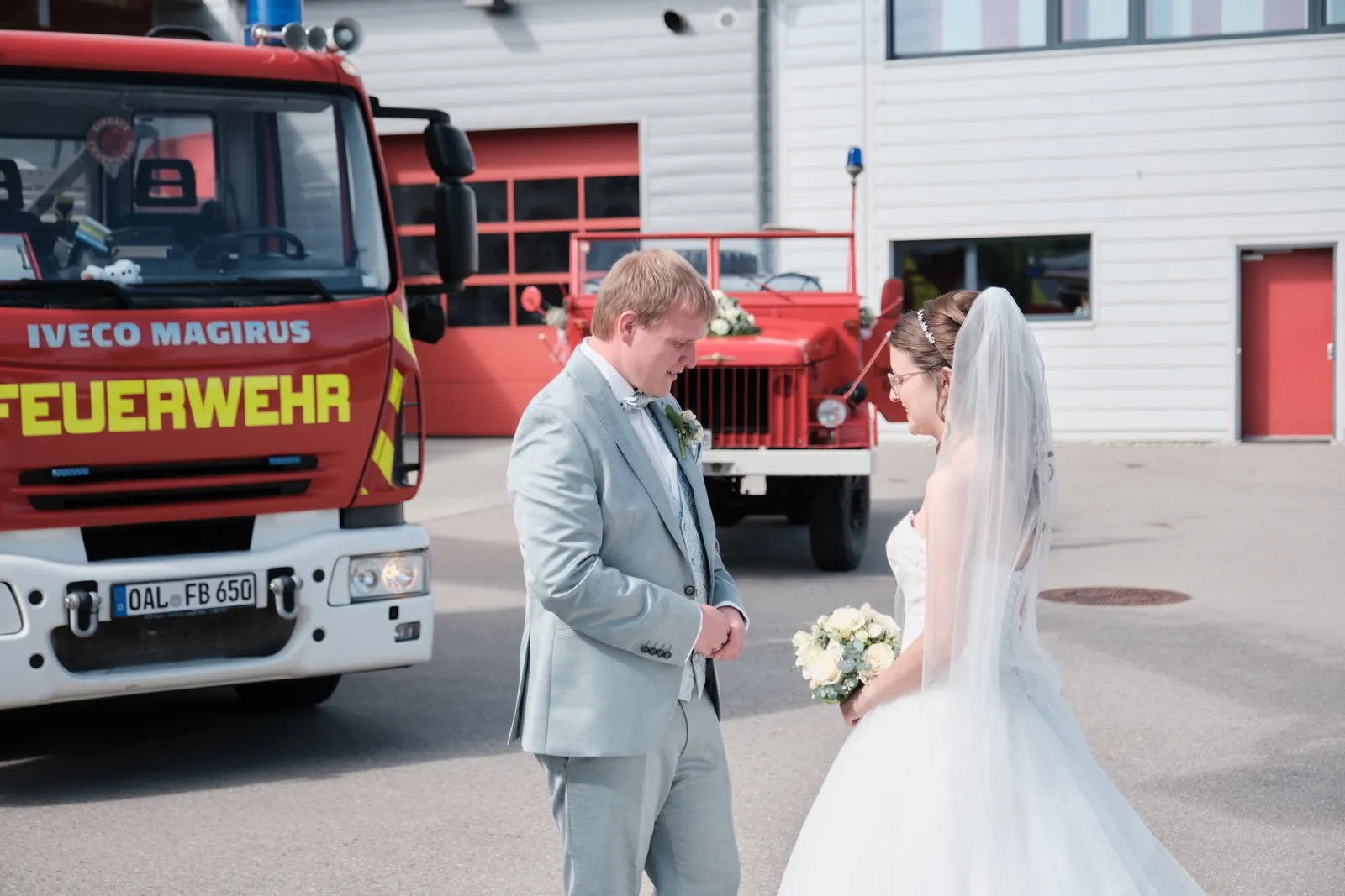 Markus und Ronja umarmen sich zwischen den Fahrzeugen – Hochzeit Ronja & Markus, Feuerwehrhaus Buchloe