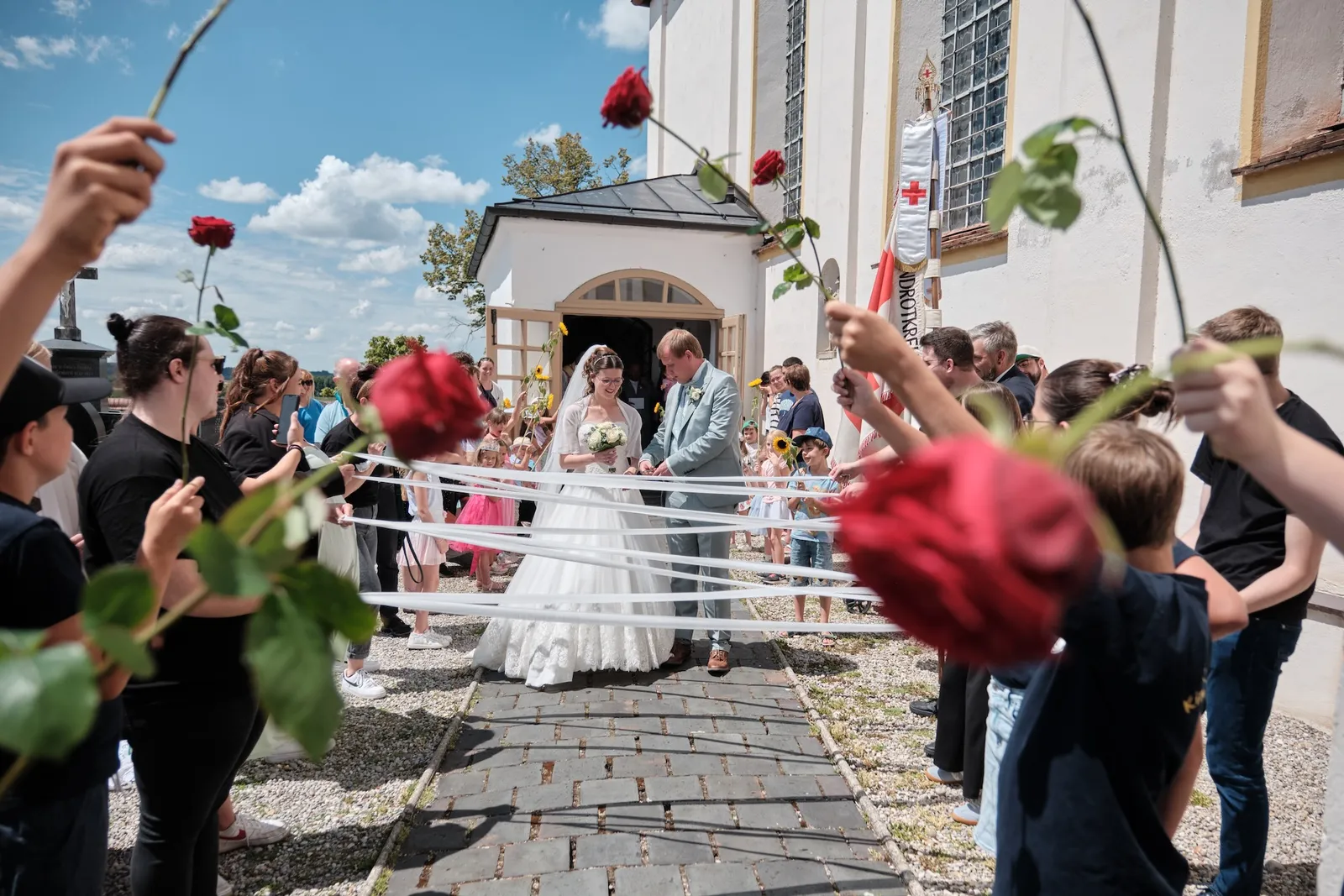 Rote Rosen fliegen über dem Brautpaar beim Auszug – Hochzeit Ronja & Markus, Buchloe