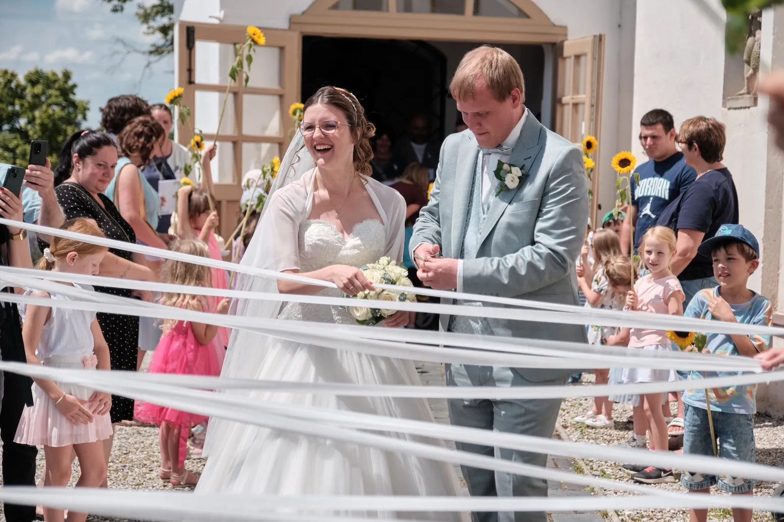 Brautpaar im Bänderspalier vor dem Kirchenportal – Hochzeit Ronja & Markus, Buchloe