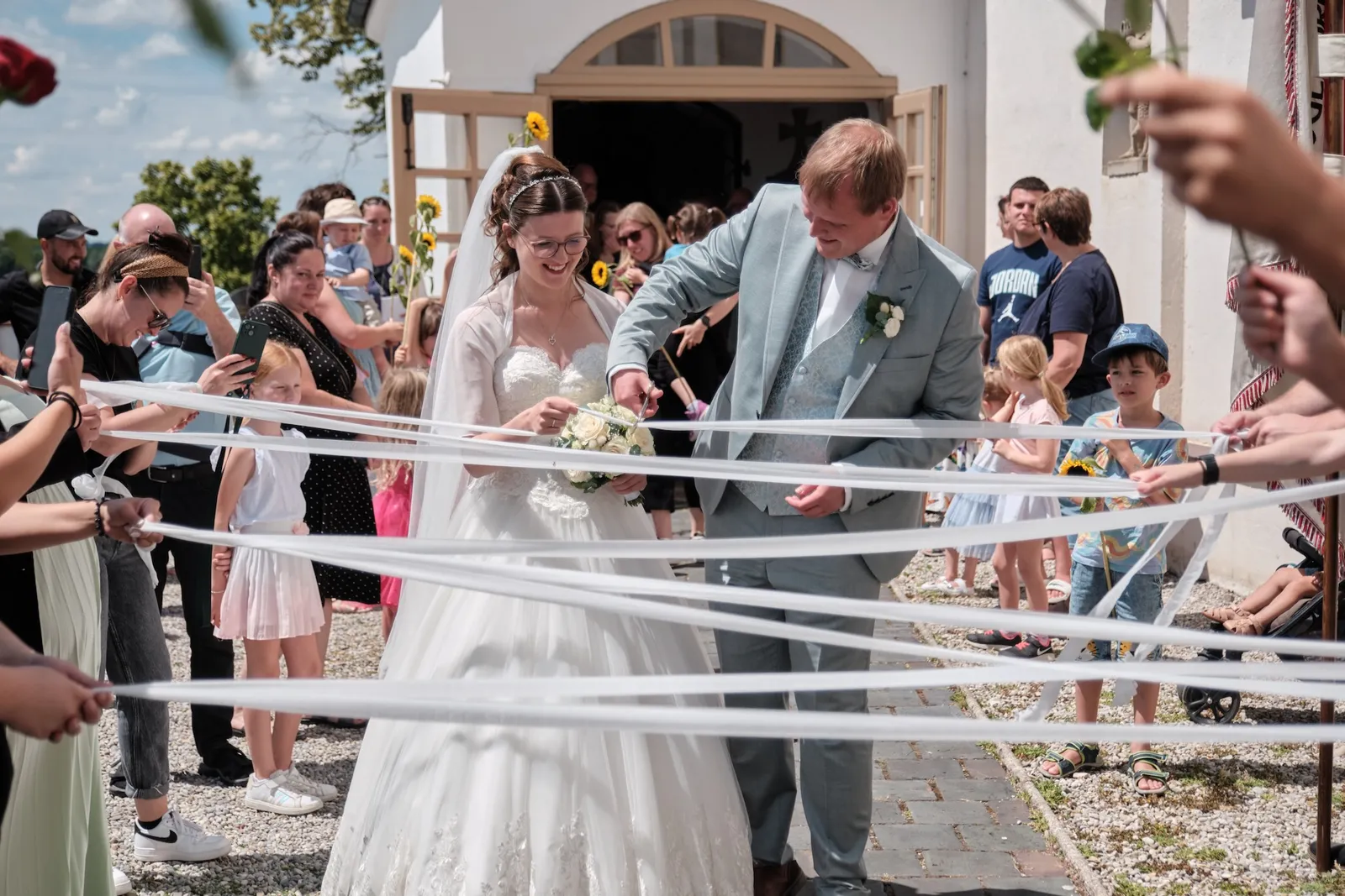 Ronja und Markus gehen durch das Spalier aus Bändern – Hochzeit Ronja & Markus, Buchloe