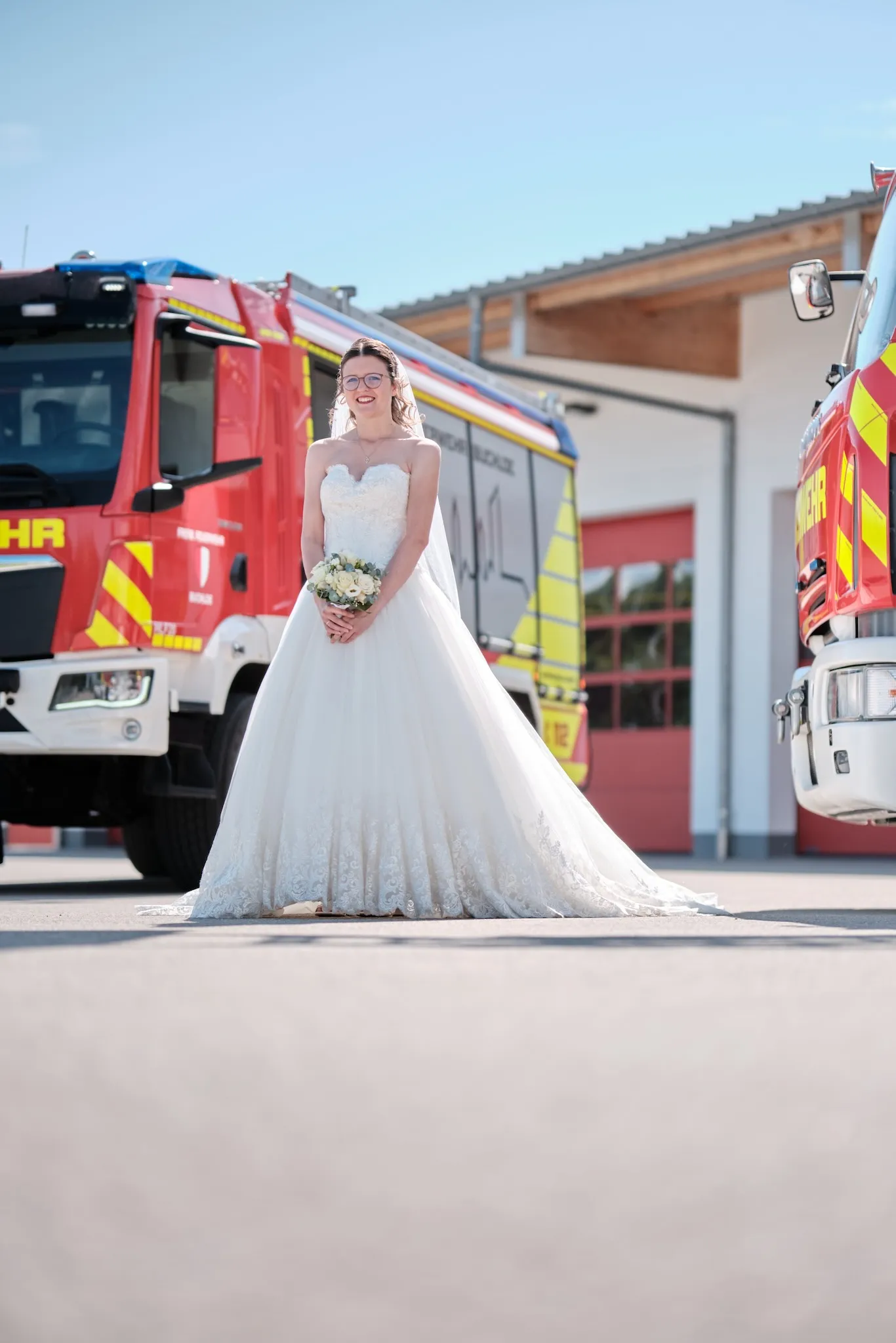 Ronja steht mit ihrem Brautstrauß vor einem Feuerwehrfahrzeug – Hochzeit Ronja & Markus, Feuerwehrhaus Buchloe