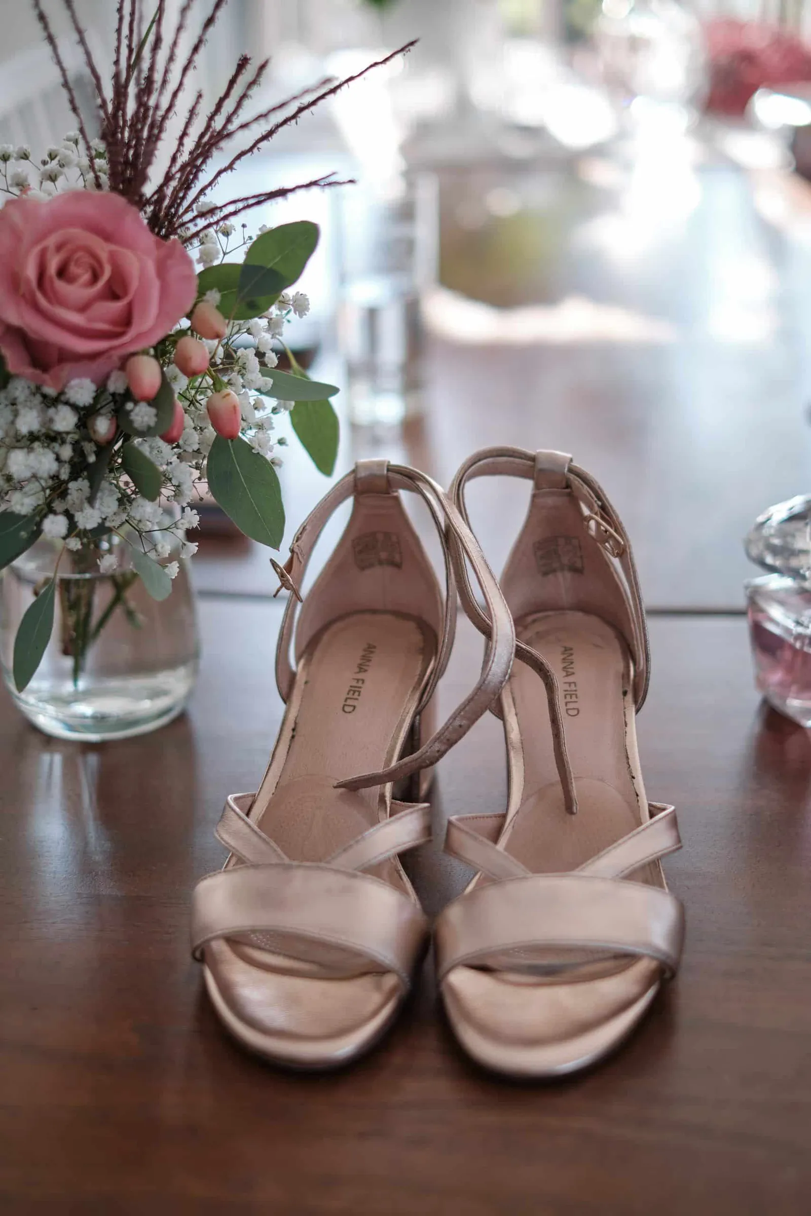 Roséfarbene Brautschuhe auf einem Tisch neben einer Blumenvase – Hochzeit Charly & Moritz, Herrenhaus Bannacker