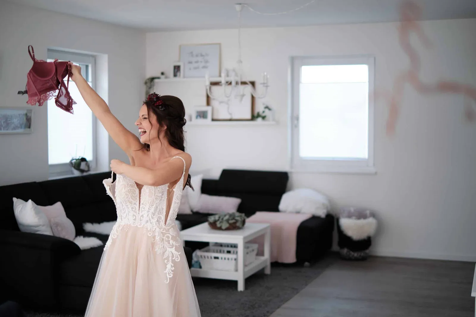 Braut im Kleid schwenkt lachend ein Tuch im Wohnzimmer – Hochzeit Charly & Moritz, Herrenhaus Bannacker