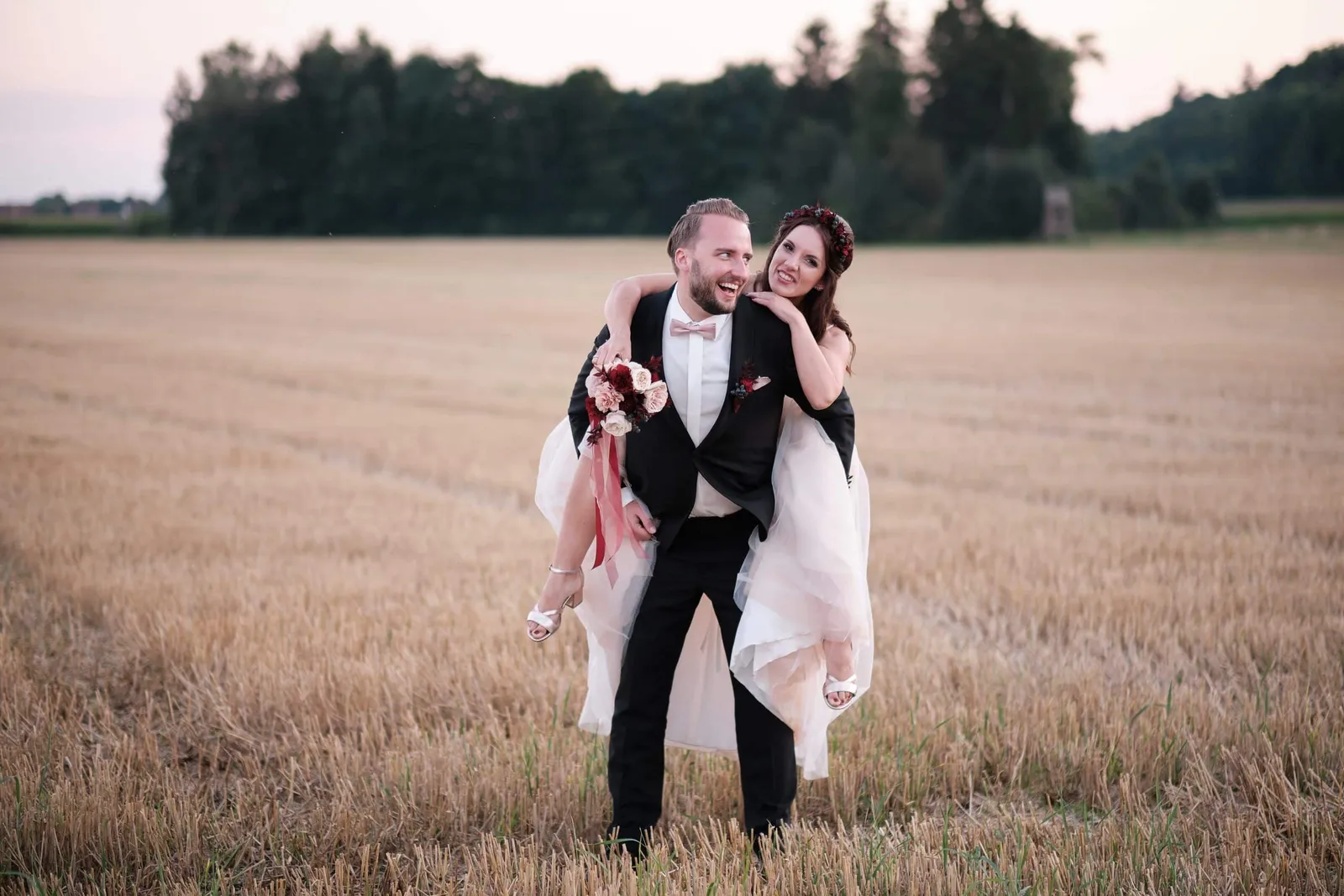 Bräutigam trägt die Braut huckepack durch ein Stoppelfeld – Hochzeit Charly & Moritz