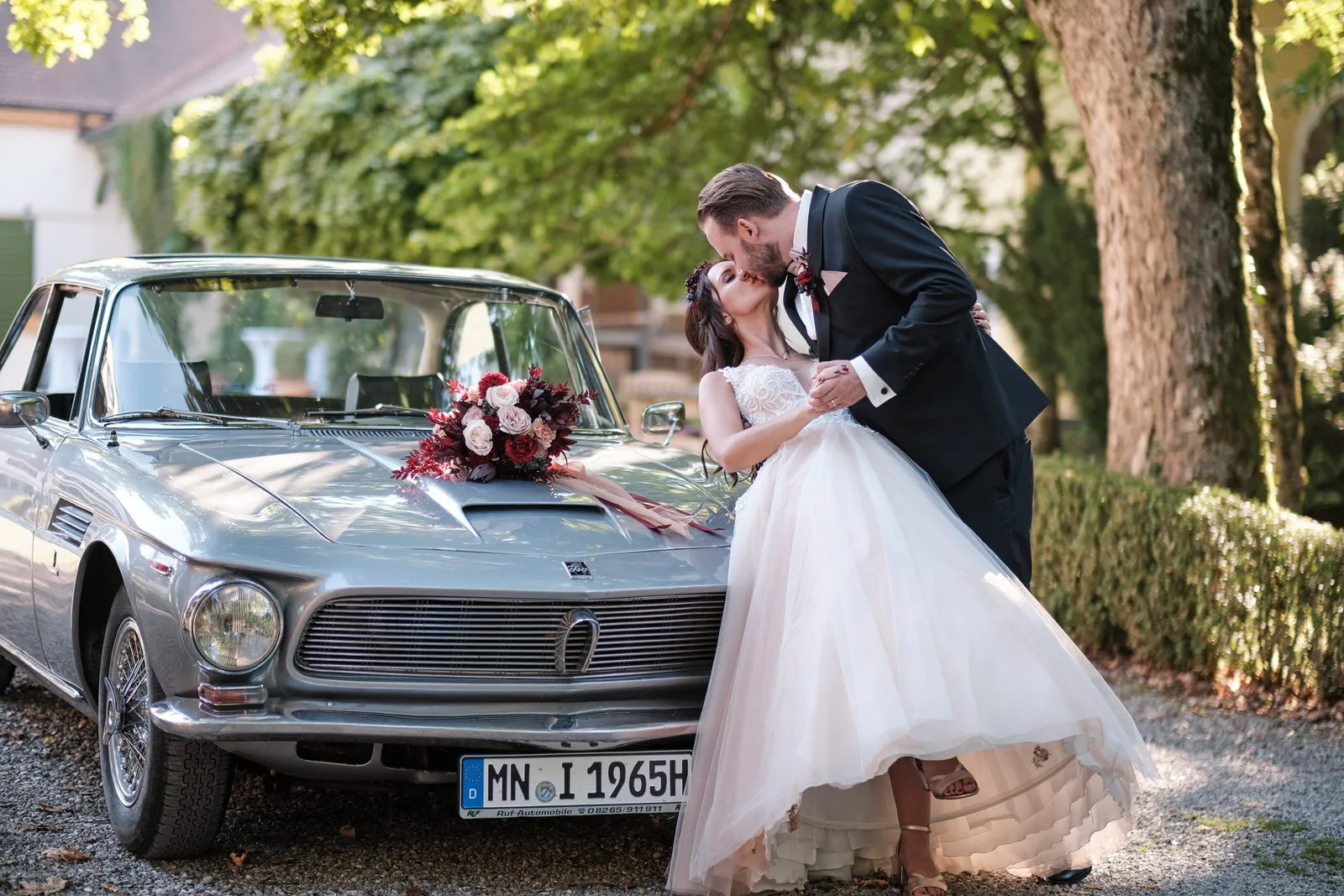 Brautpaar küsst sich vor einem silbernen Oldtimer – Hochzeit Charly & Moritz