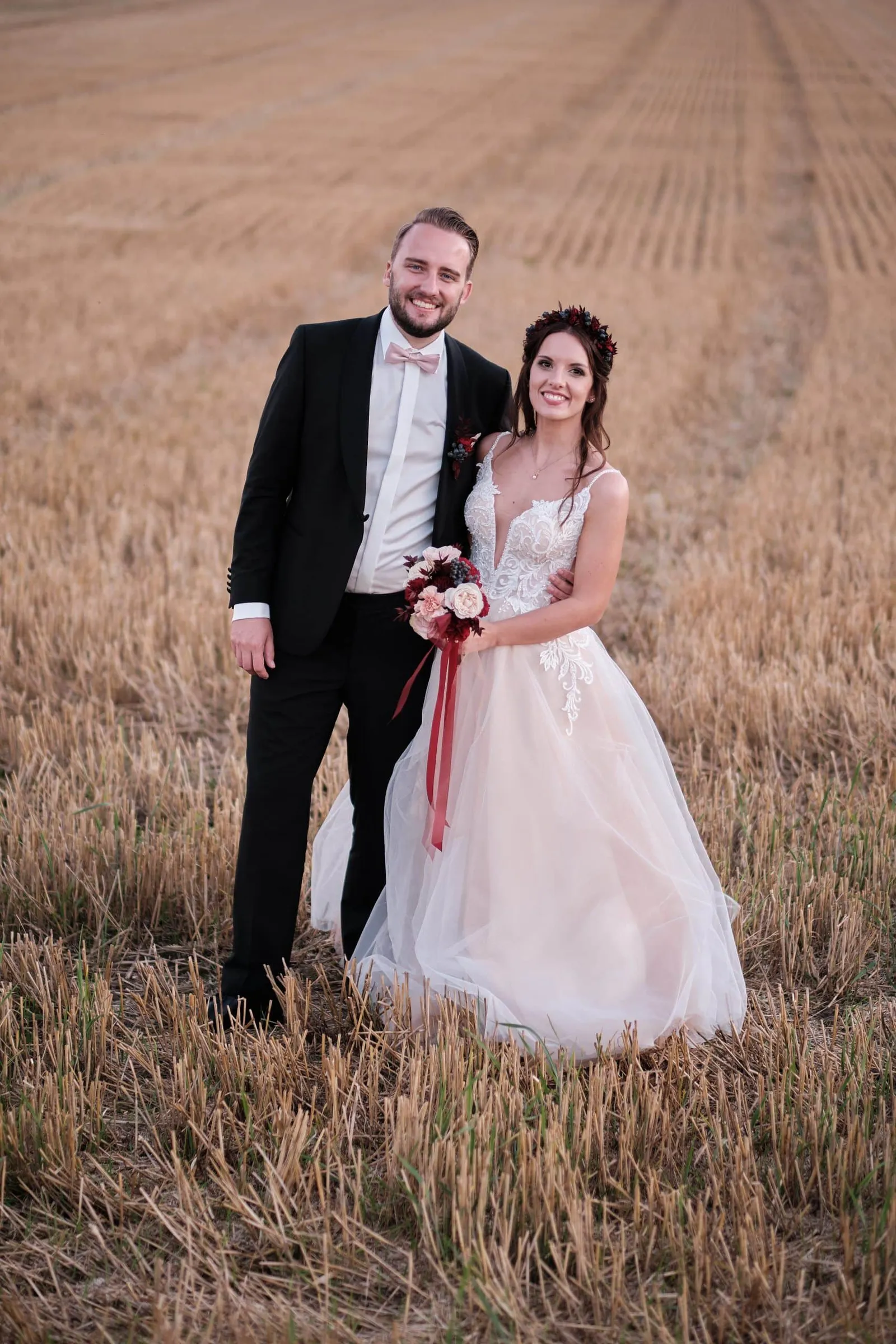 Brautpaar steht lächelnd in einem Stoppelfeld – Hochzeit Charly & Moritz