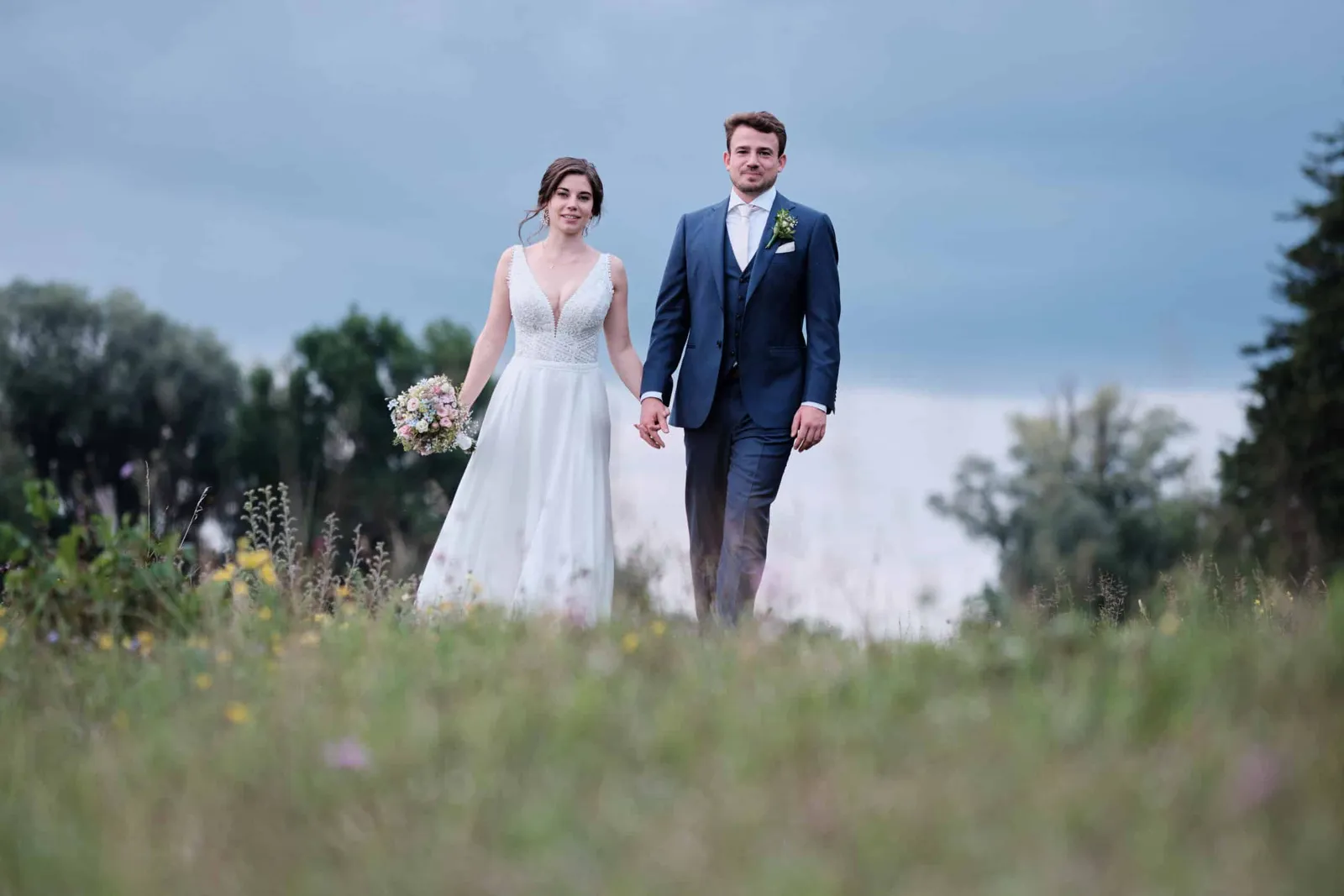 Brautpaar läuft Hand in Hand über eine Wiese auf die Kamera zu – Hochzeit Hanna & Tobi