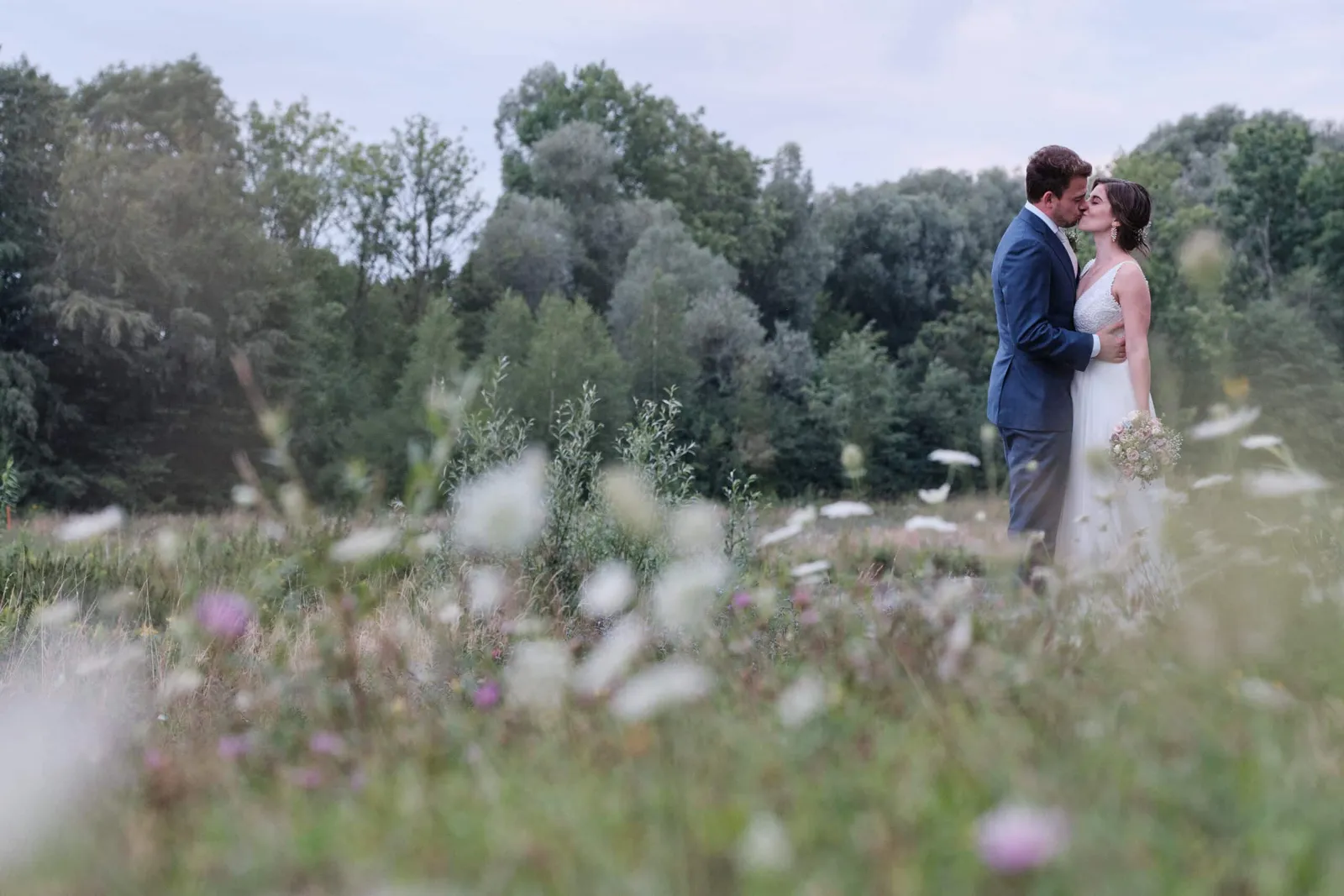 Brautpaar küsst sich zwischen weißen Wildblumen – Hochzeit Hanna & Tobi