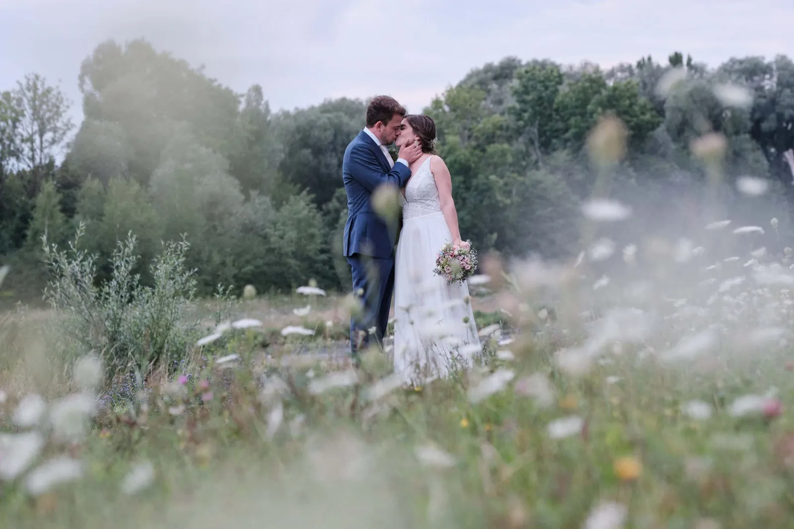 Bräutigam küsst die Braut auf die Schläfe in einer Blumenwiese – Hochzeit Hanna & Tobi