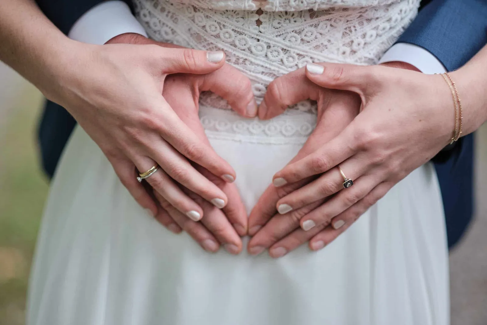 Hände des Brautpaars mit Eheringen formen ein Herz vor dem Brautkleid – Hochzeit Hanna & Tobi, Herrenhaus Bannacker