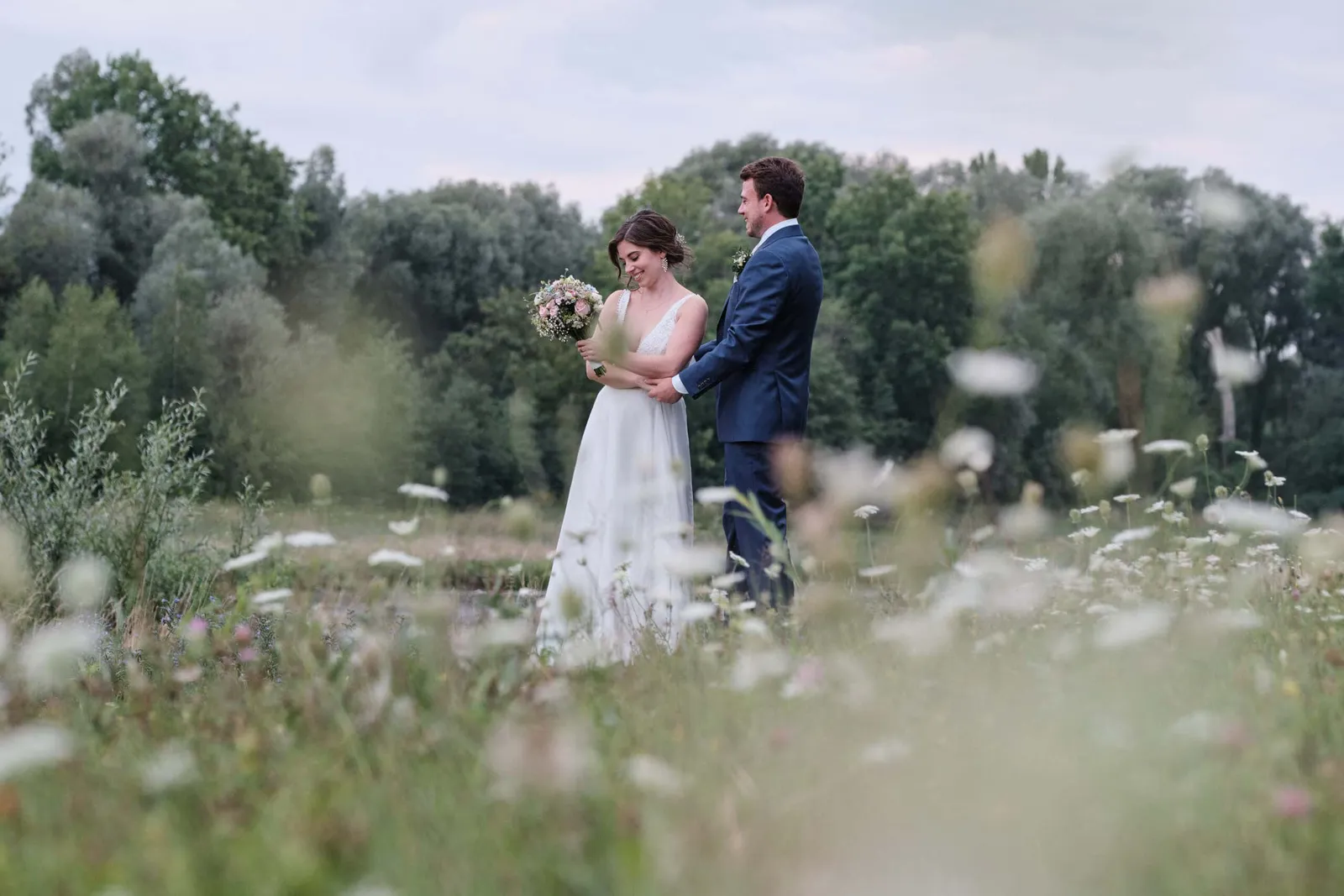 Brautpaar steht einander zugewandt hinter blühenden Wildblumen – Hochzeit Hanna & Tobi