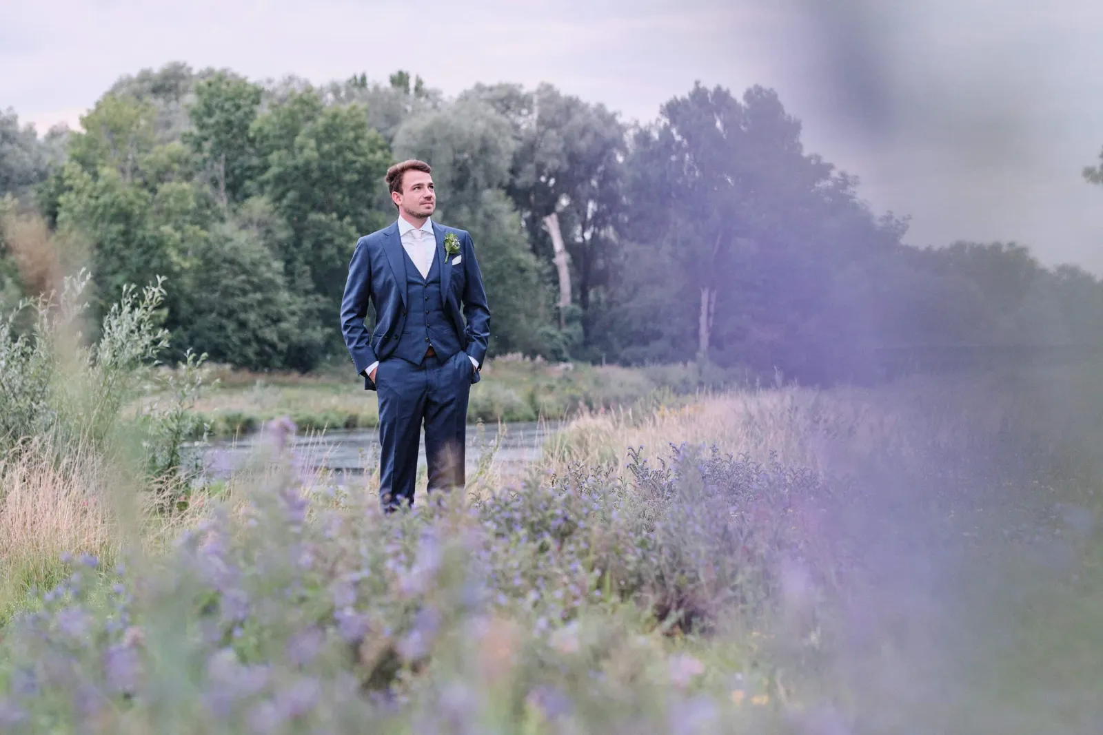 Bräutigam mit Händen in den Taschen auf einer Wiese am Wasser – Hochzeit Hanna & Tobi