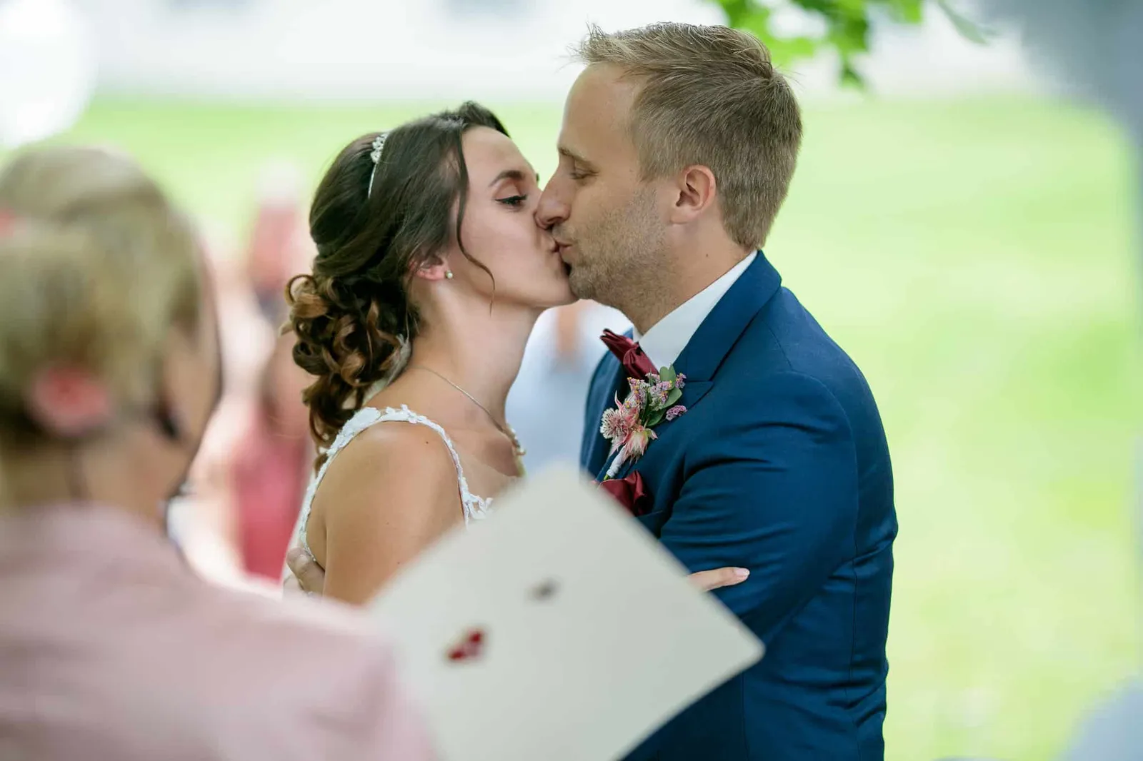 Brautpaar küsst sich bei der freien Trauung, Traurednerin im Vordergrund – Hochzeit Julia & Phil, Herrenhaus Bannacker