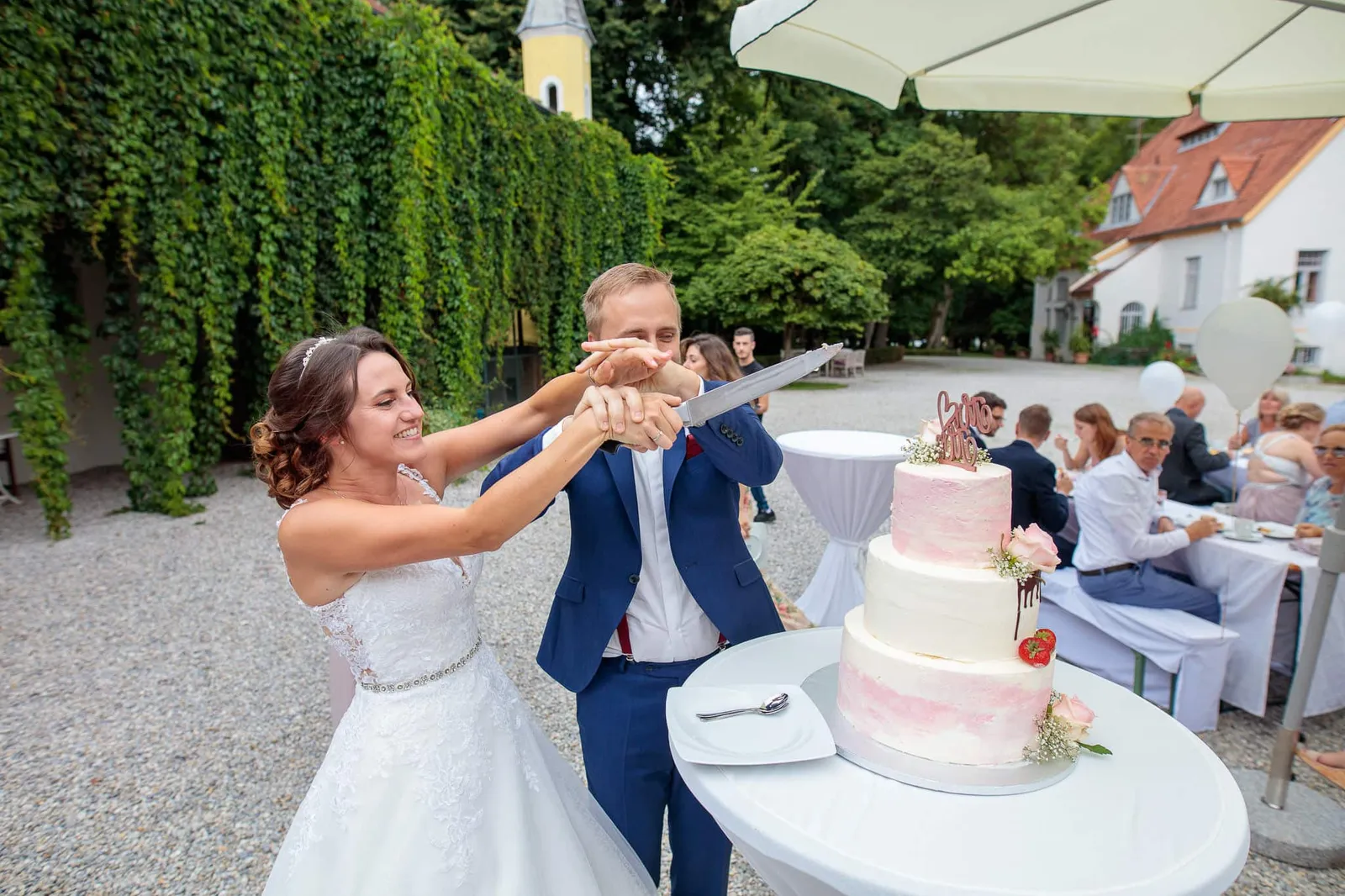 Brautpaar schneidet gemeinsam die Hochzeitstorte im Innenhof an – Hochzeit Julia & Phil, Herrenhaus Bannacker