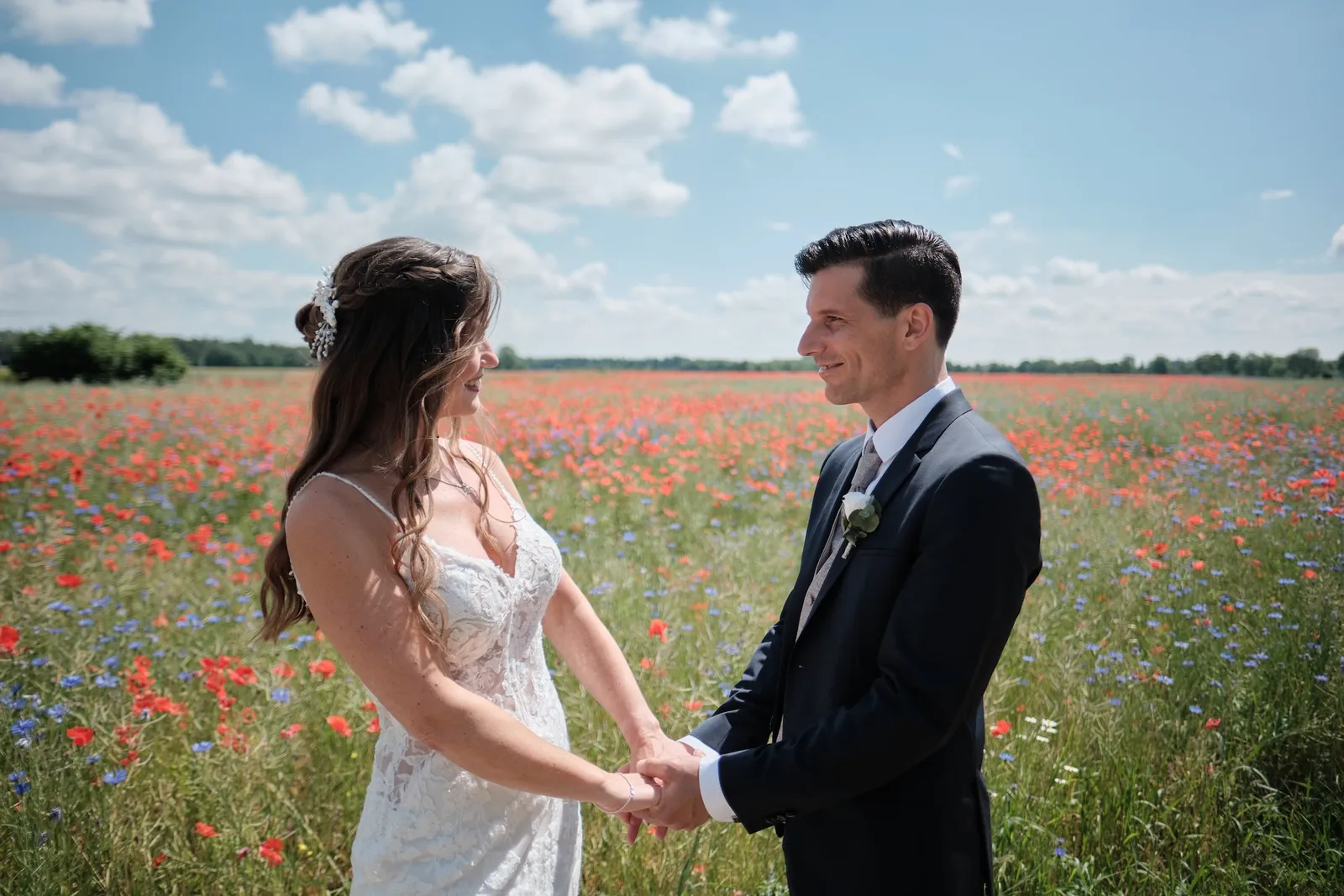 Brautpaar hält Händchen im Mohnfeld und schaut sich an – Hochzeit Markus & Tanja, Mohnfeld bei Königsbrunn