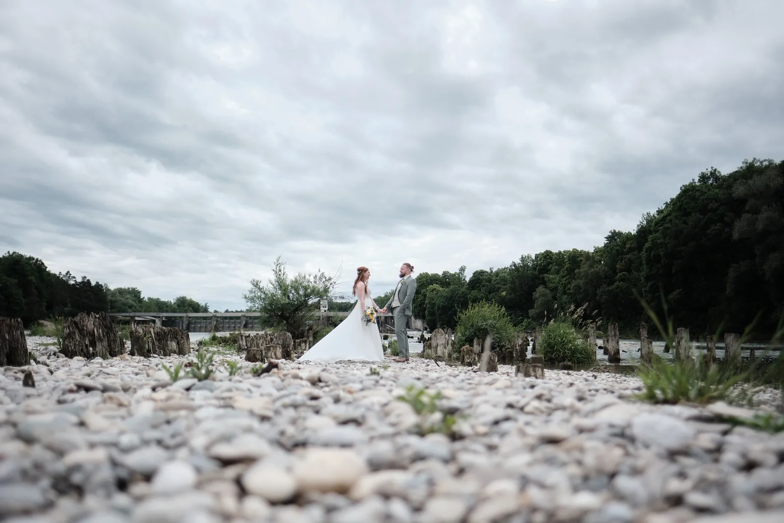Brautpaar klein in der weiten Kieslandschaft am Lech unter bewölktem Himmel – Hochzeit Svenja & Markus, Hochablass Augsburg