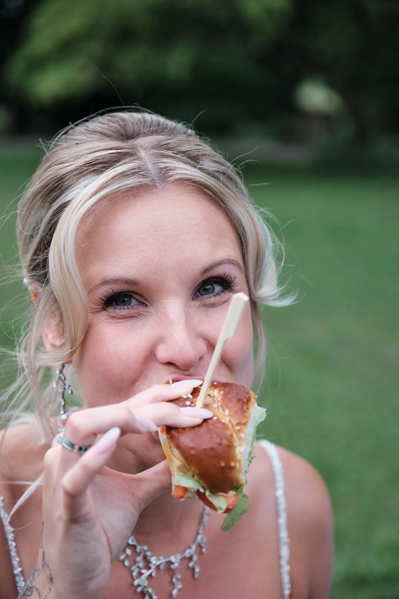 Celina beißt lachend in einen Burger beim Empfang im Garten – Hochzeit Celina & Denny, Parkhotel Schmid Adelsried