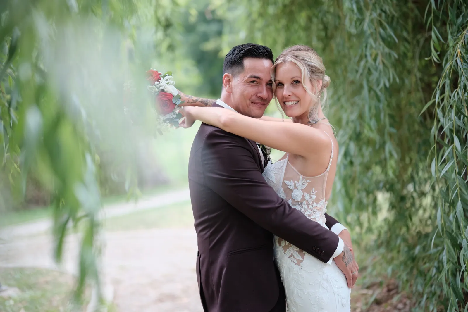 Brautpaar umarmt sich zwischen den Zweigen einer Trauerweide im Park – Hochzeit Celina & Denny, Parkhotel Schmid Adelsried