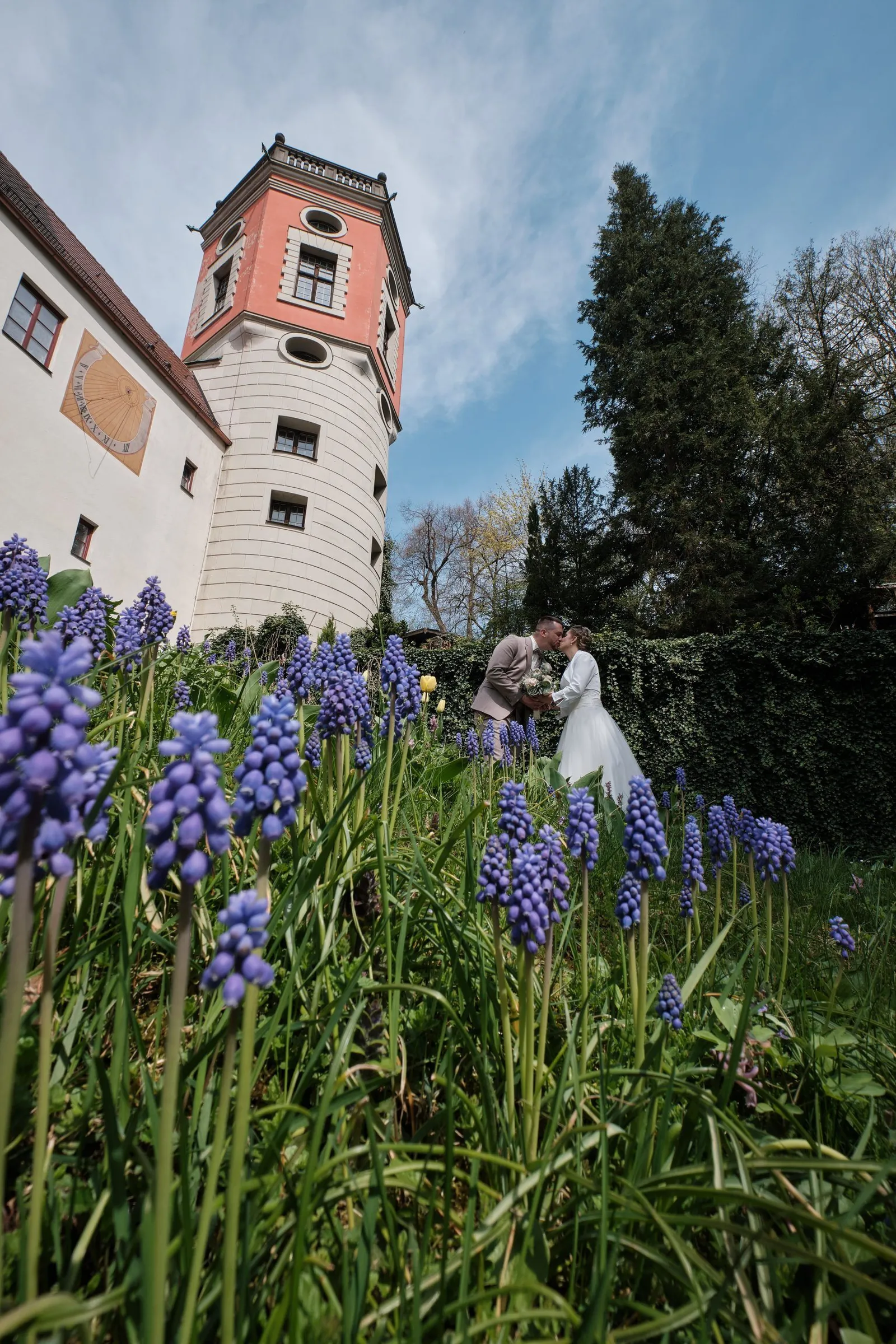 Brautpaar vor einem Turm, lila Traubenhyazinthen im Vordergrund – Hochzeit Andi & Betti