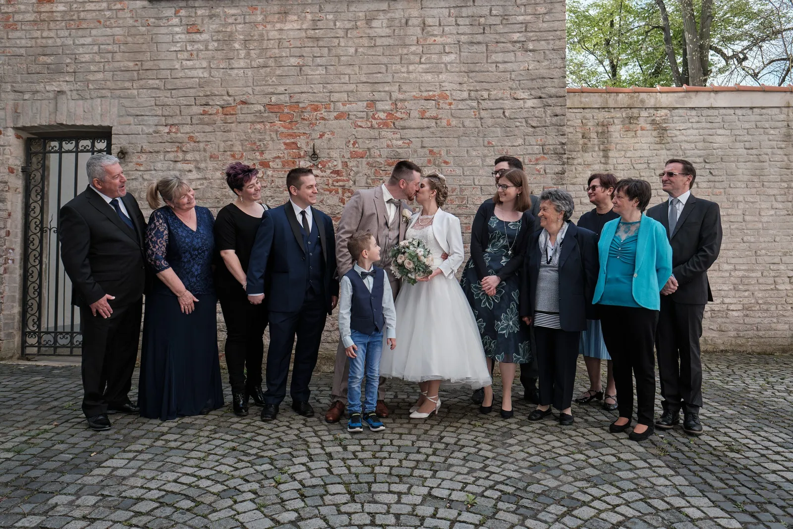 Brautpaar mit Familie auf Kopfsteinpflaster vor einer Backsteinmauer – Hochzeit Andi & Betti, Schaezlerpalais