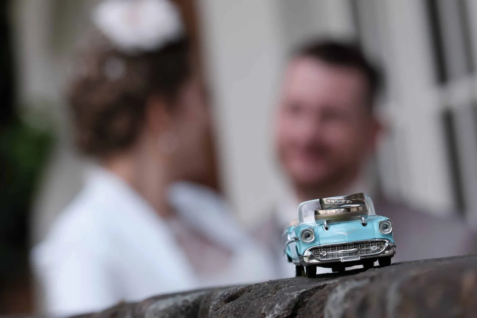 Eheringe auf einem Modellauto, Brautpaar unscharf im Hintergrund – Hochzeit Andi & Betti, Schaezlerpalais