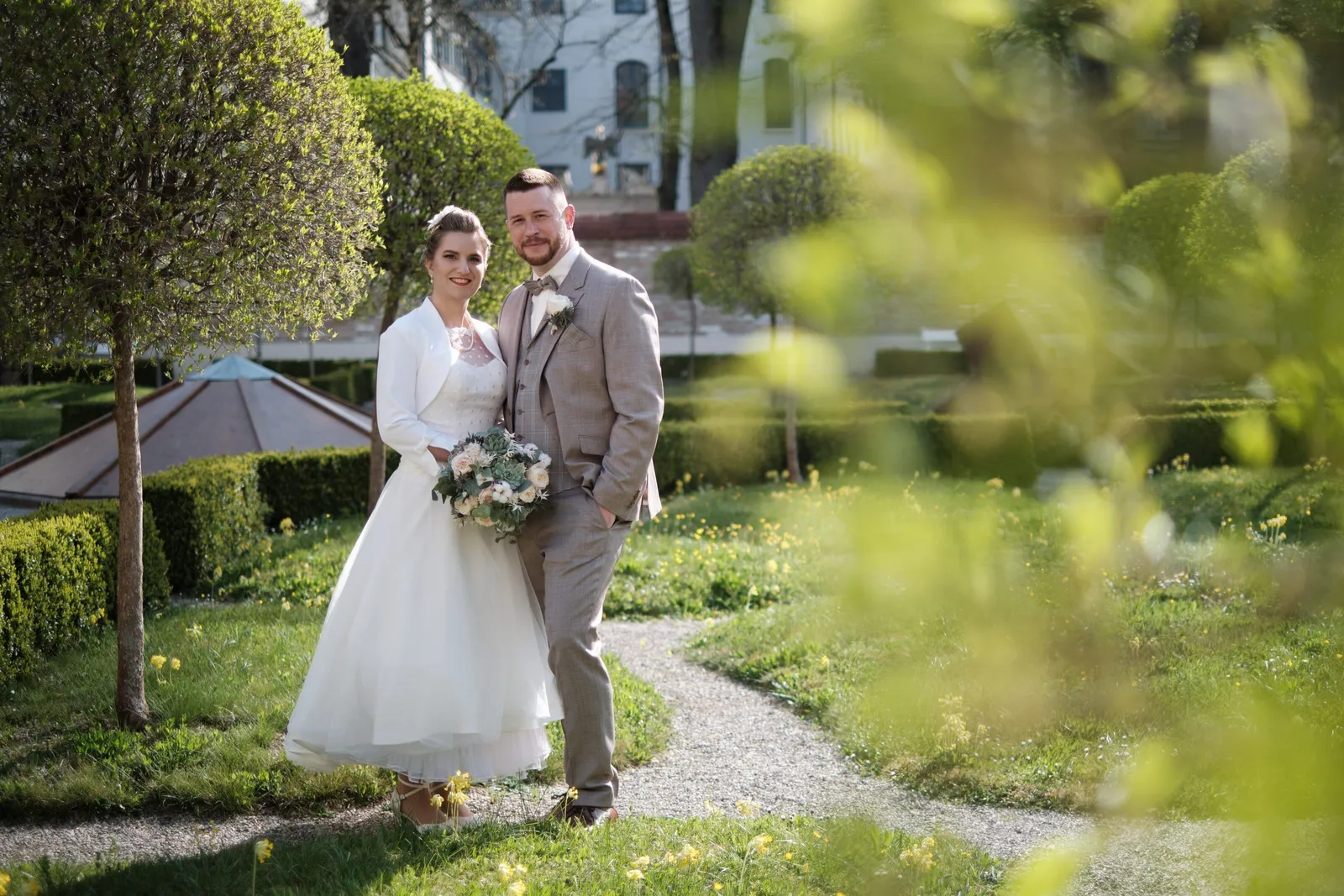Brautpaar in einem Garten, unscharfe Blätter im Vordergrund – Hochzeit Andi & Betti