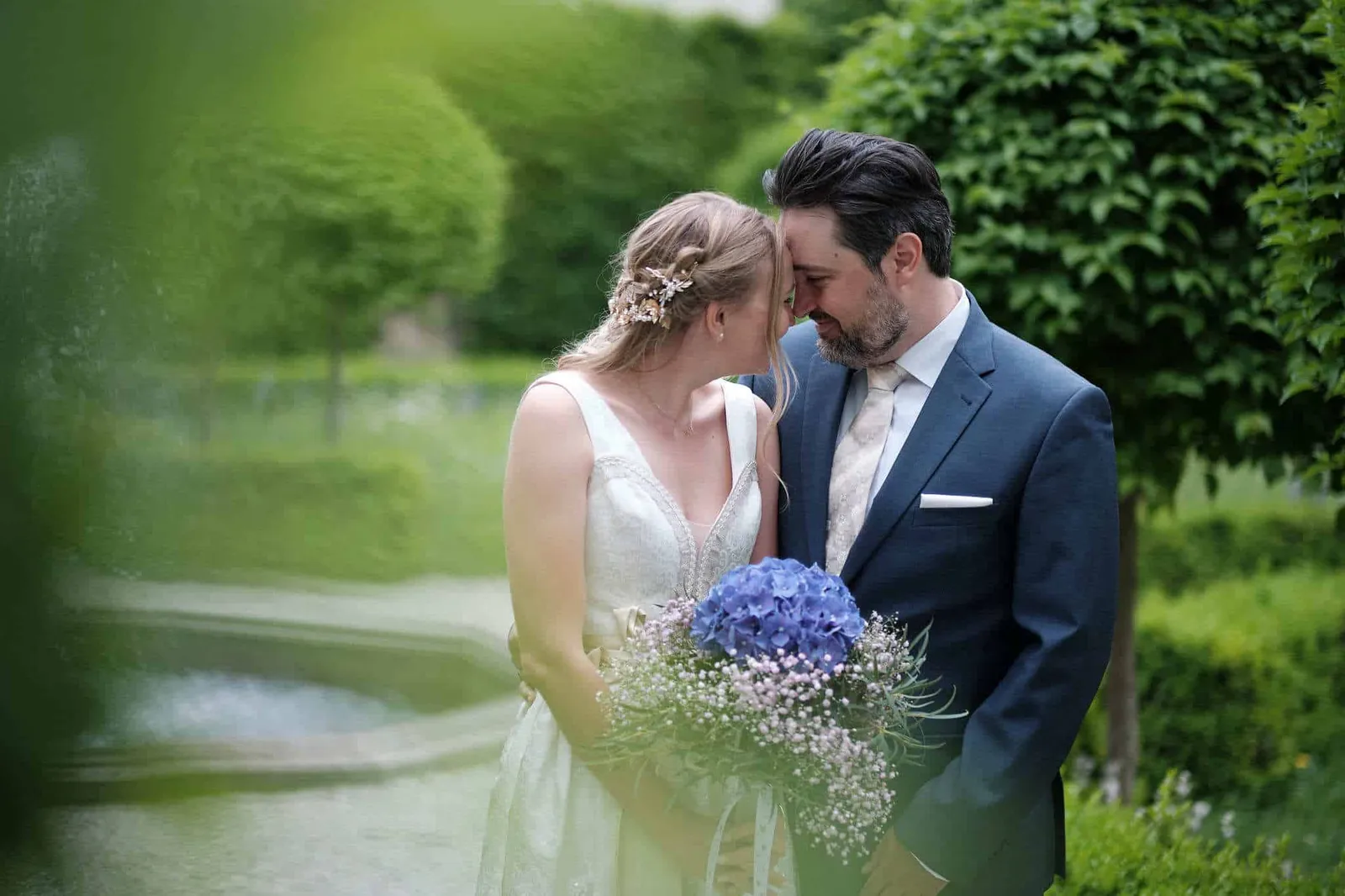 Brautpaar Stirn an Stirn mit blauem Hortensienstrauß im Garten – Hochzeit Katharina & Christian