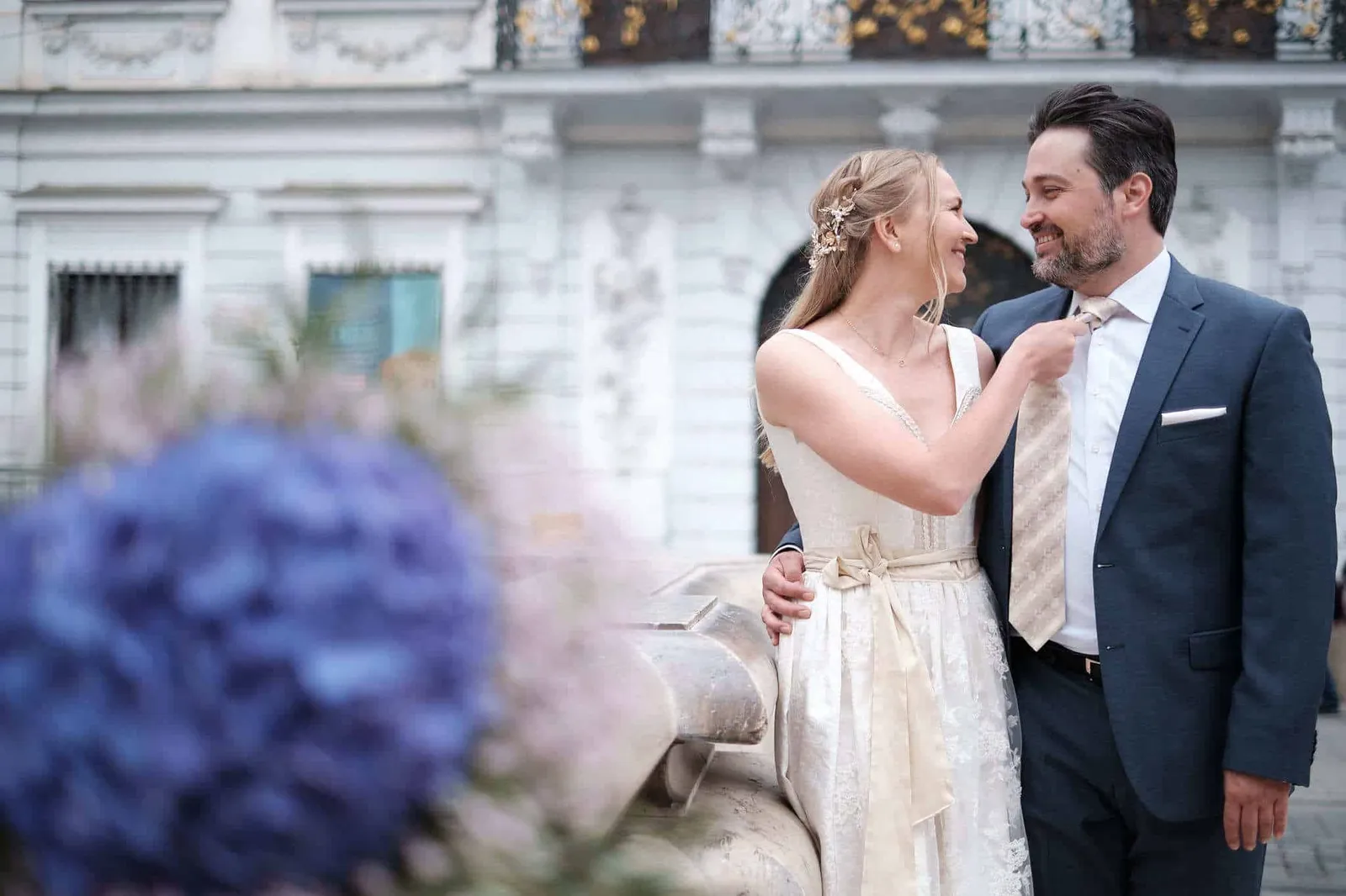 Brautpaar vor einer Stuckfassade, blauer Brautstrauß im Vordergrund – Hochzeit Katharina & Christian