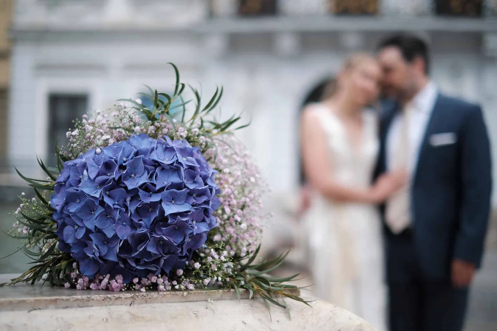 Blauer Hortensienstrauß, Brautpaar unscharf im Hintergrund – Hochzeit Katharina & Christian, Schaezlerpalais