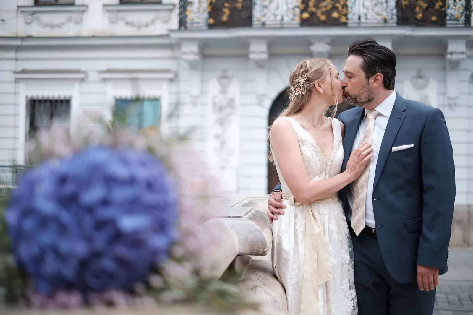 Brautpaar küsst sich vor einer Stuckfassade, Strauß im Vordergrund – Hochzeit Katharina & Christian