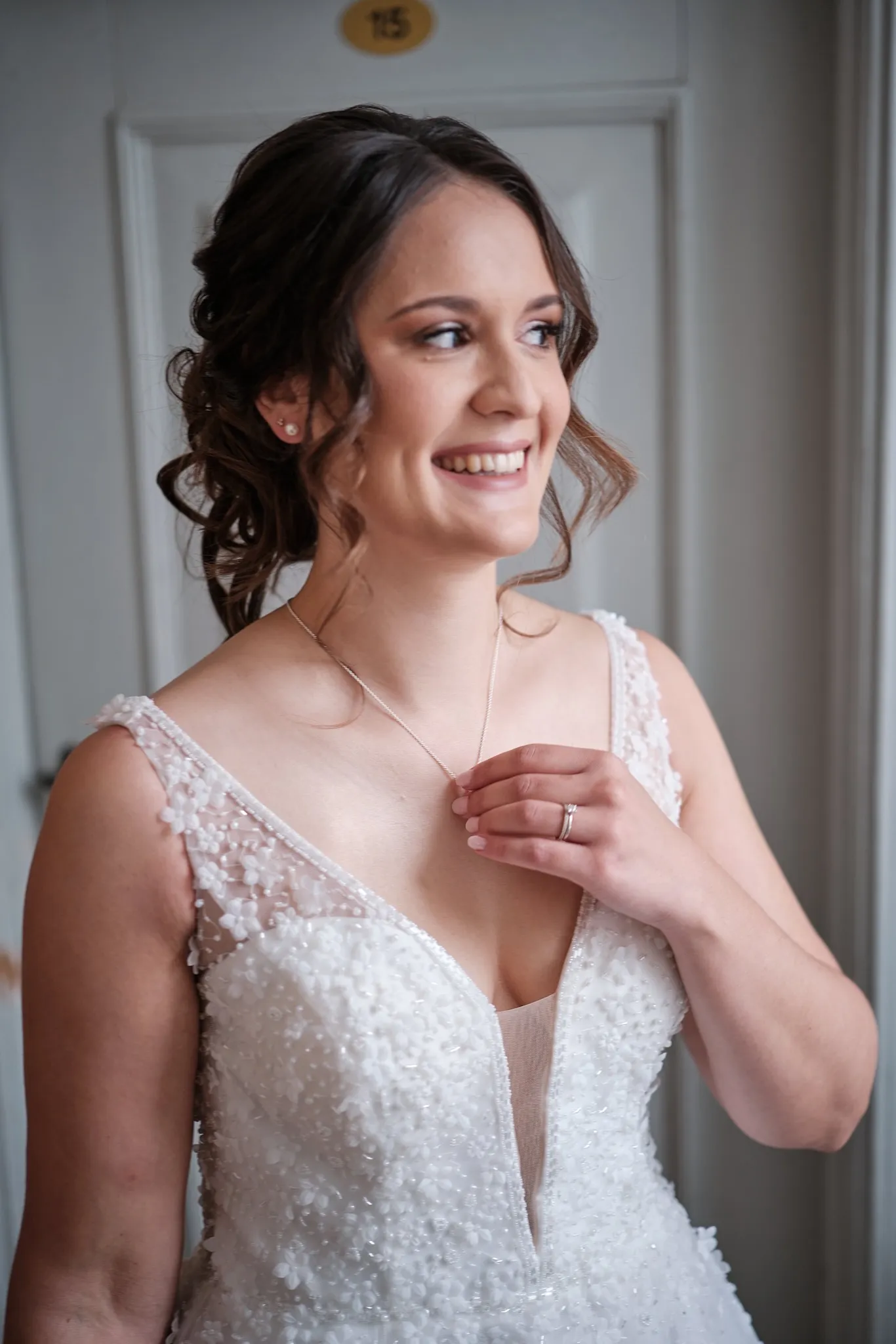 Braut im Kleid legt lächelnd die Kette an – Hochzeit Barbara & Christian, Schloss Neuburg a.d. Kammel