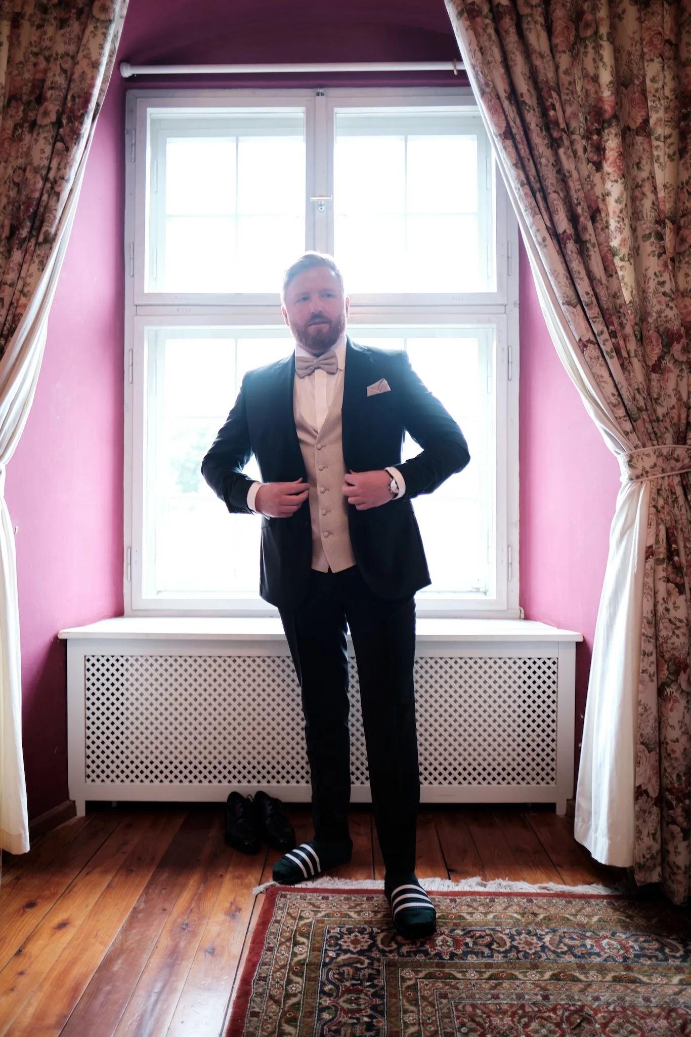 Bräutigam fertig angezogen am Fenster, rosa Vorhänge im Hintergrund – Hochzeit Barbara & Christian, Schloss Neuburg a.d. Kammel