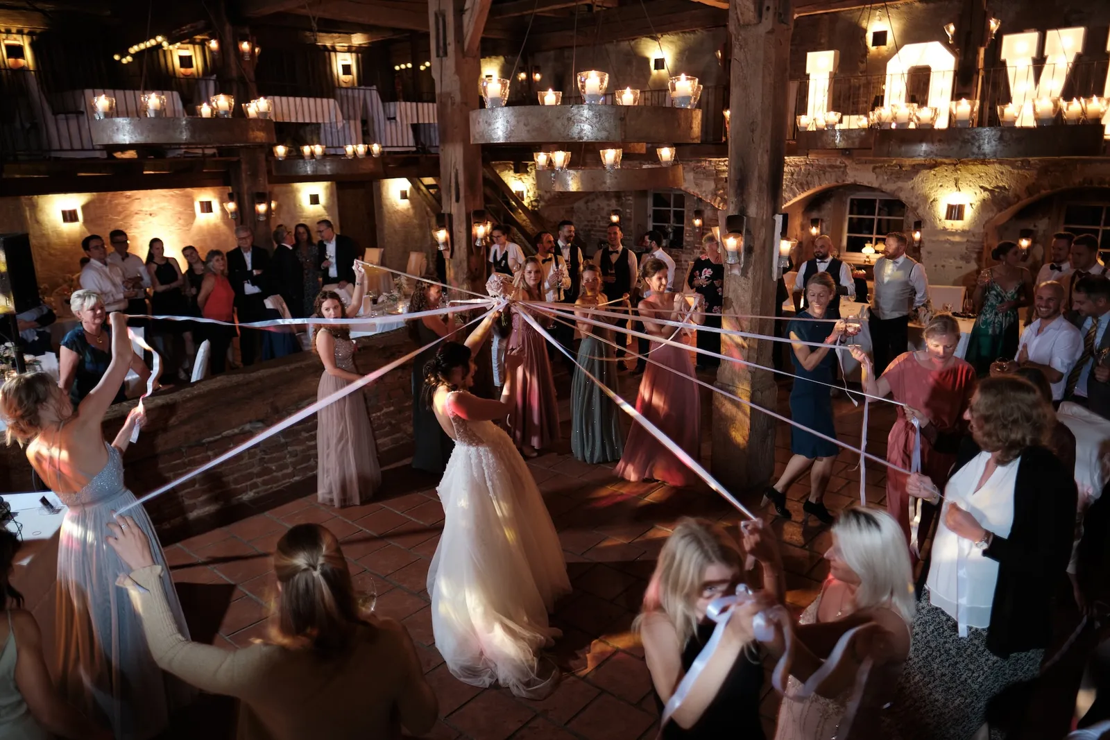 Bänder-Spiel mit tanzenden Gästen, LOVE-Schriftzug im Hintergrund – Hochzeit Barbara & Christian, Schloss Neuburg a.d. Kammel