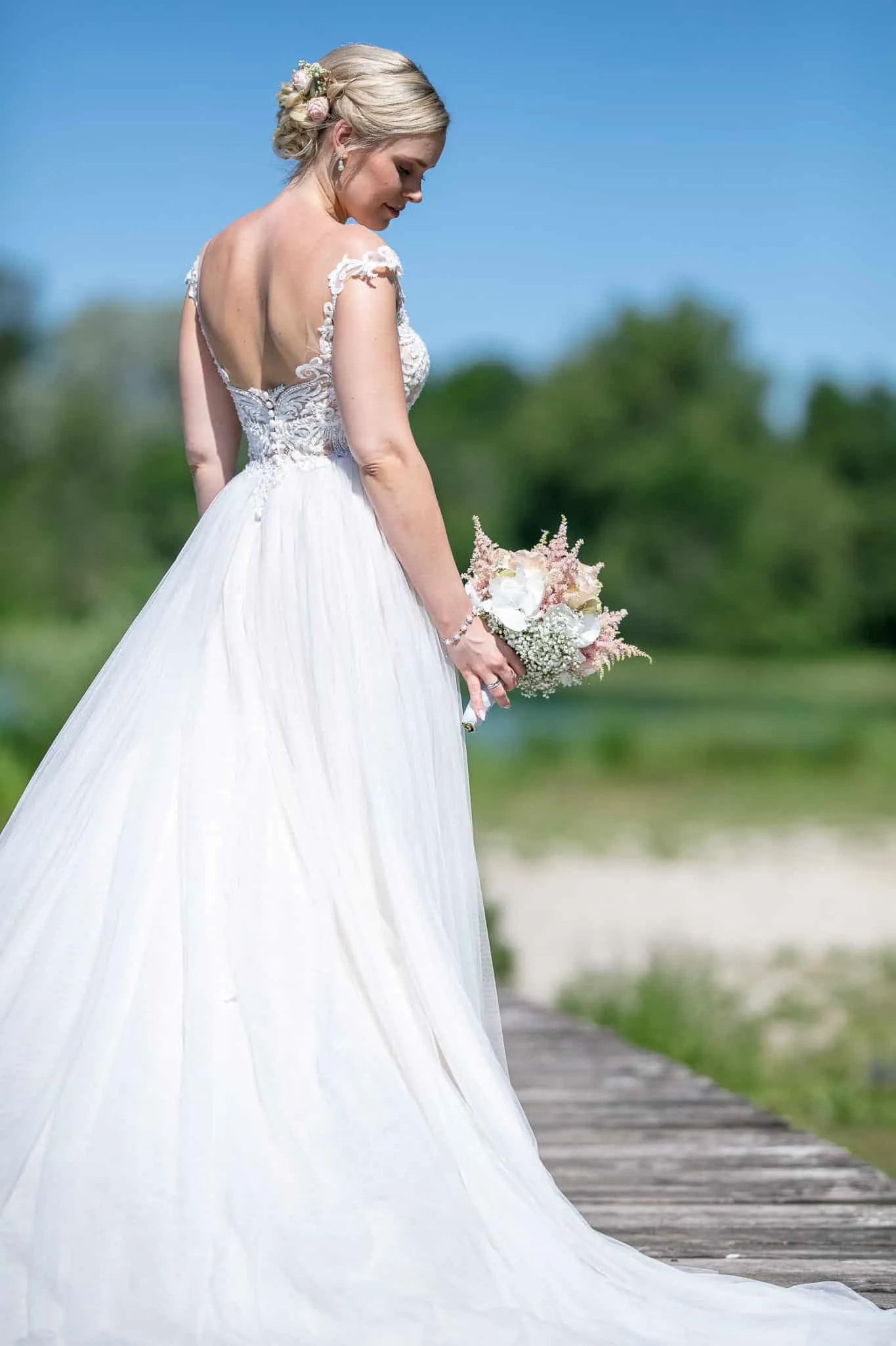 Braut von hinten mit Rückenausschnitt und Brautstrauß auf dem Steg – Hochzeit Andreas & Nicole