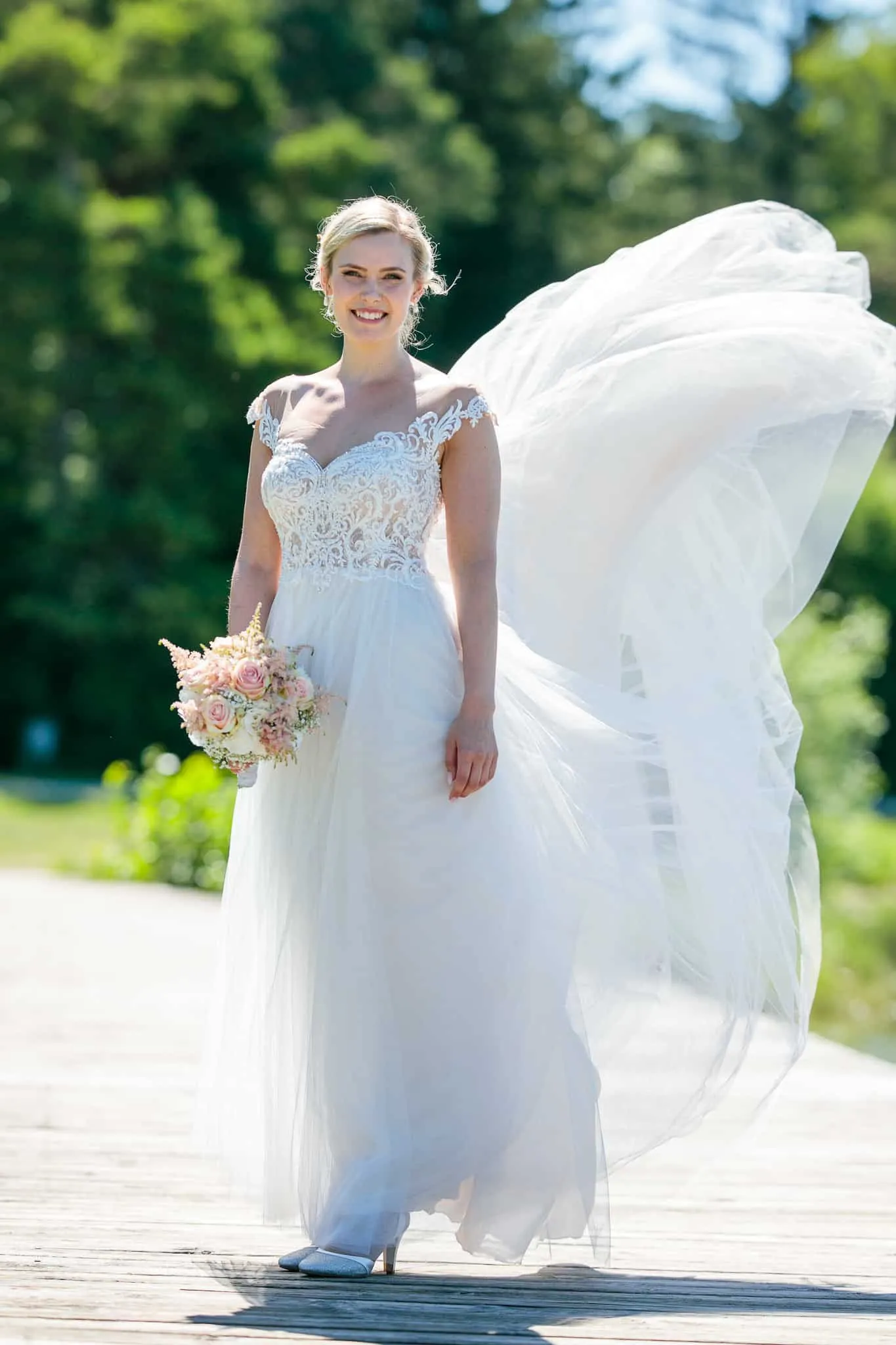 Braut lächelt auf dem Holzsteg, ihr Rock weht im Wind – Hochzeit Andreas & Nicole