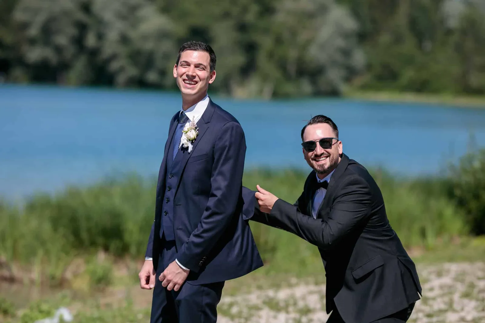Bräutigam lacht mit einem Freund mit Sonnenbrille am Seeufer – Hochzeit Andreas & Nicole, Weitmannsee