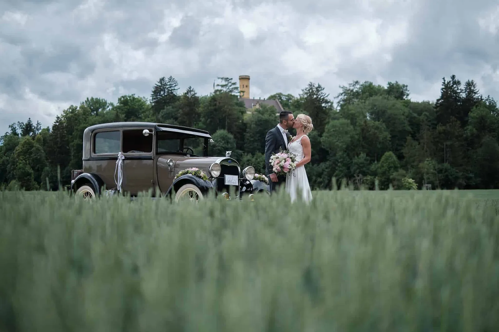 Brautpaar neben einem Oldtimer am Rand eines Getreidefelds – Hochzeit Jessie & Kosta