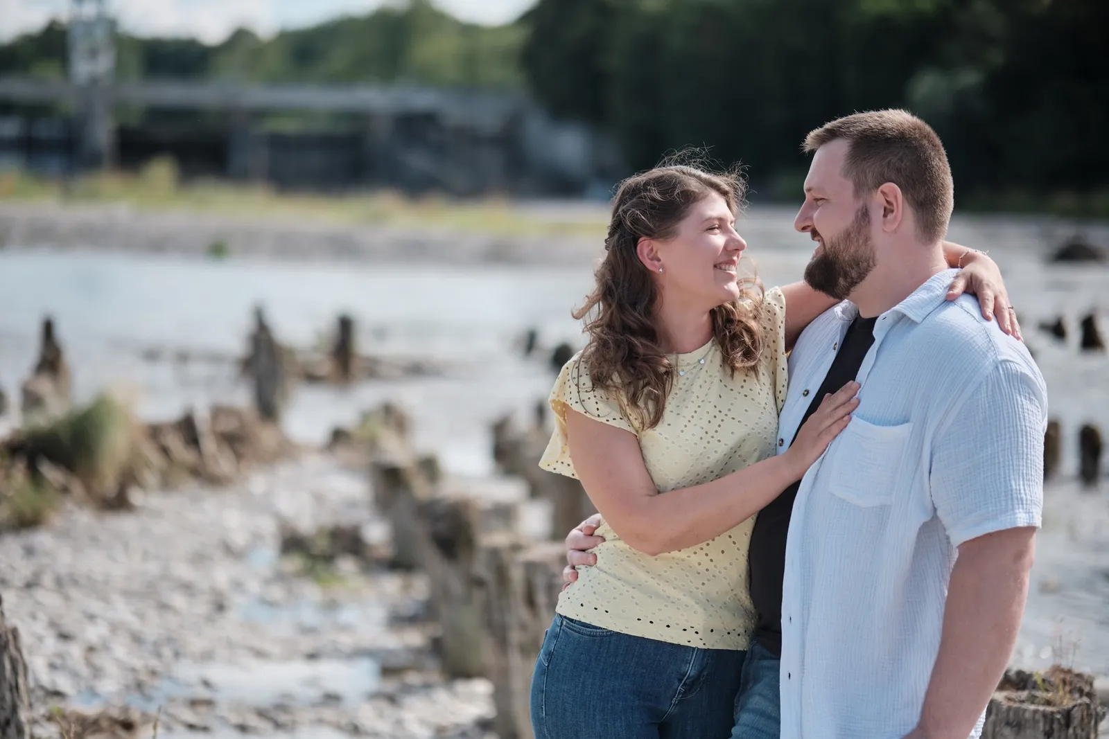 Umarmung am Holzpfahl mit weitem Blick auf die Kiesbänke und den Lech – Kennenlernshooting Matthias & Rebecca, Hochablass Augsburg