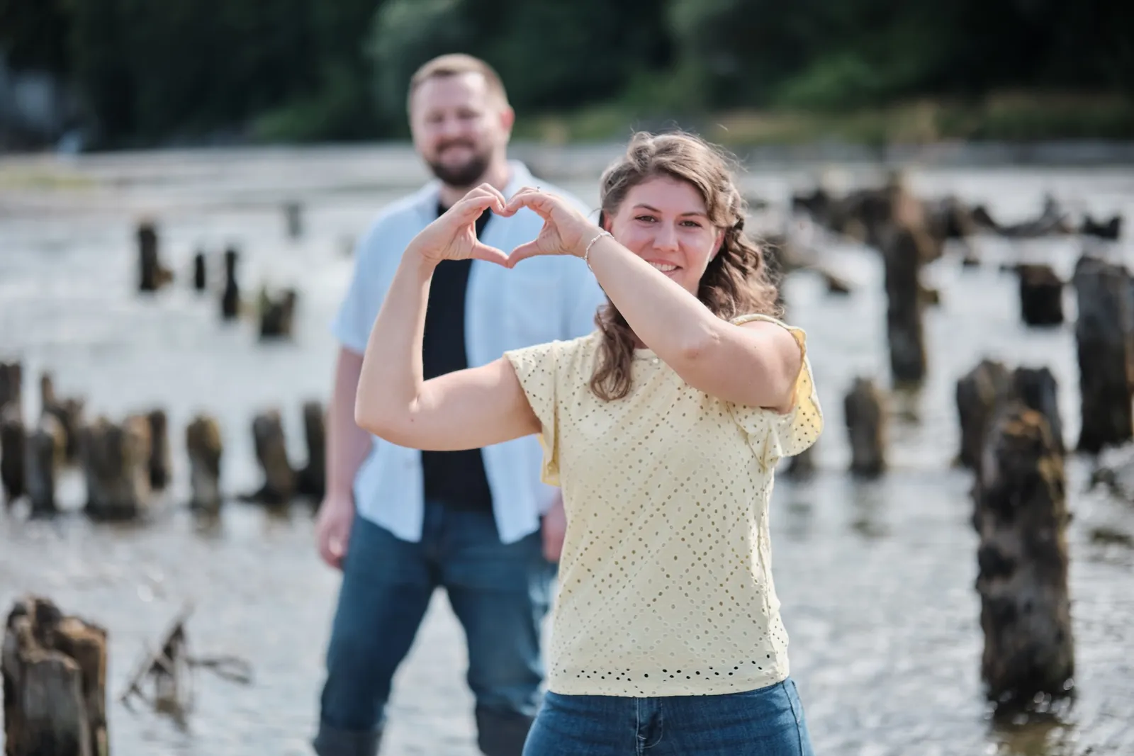 Herz-Geste mit den Händen zwischen den Holzpfählen im Lech – Kennenlernshooting Matthias & Rebecca, Hochablass Augsburg