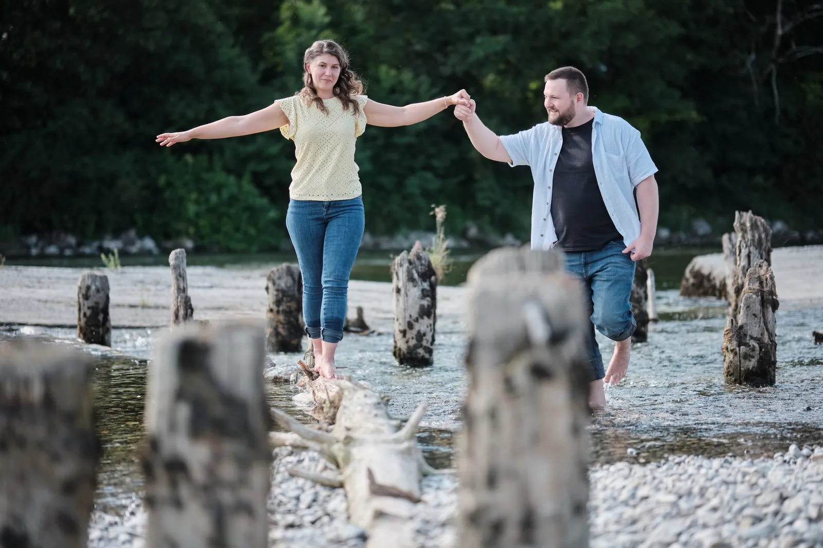 Balanceakt auf einem Baumstamm im Wasser, Arme ausgestreckt und Hand in Hand – Kennenlernshooting Matthias & Rebecca, Hochablass Augsburg