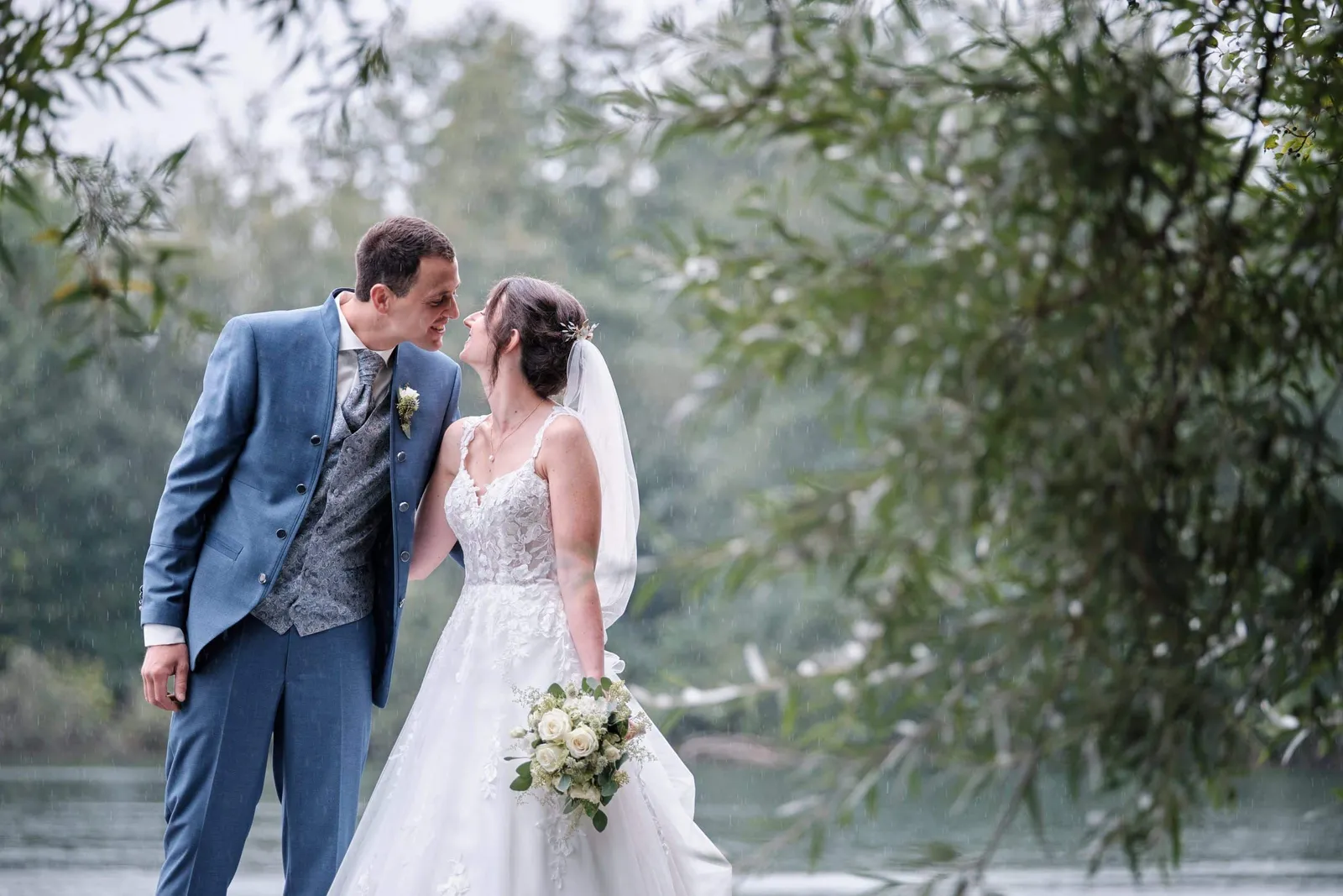 Brautpaar lächelt sich am See zwischen Weidenzweigen an – Hochzeit Christina & Manuel
