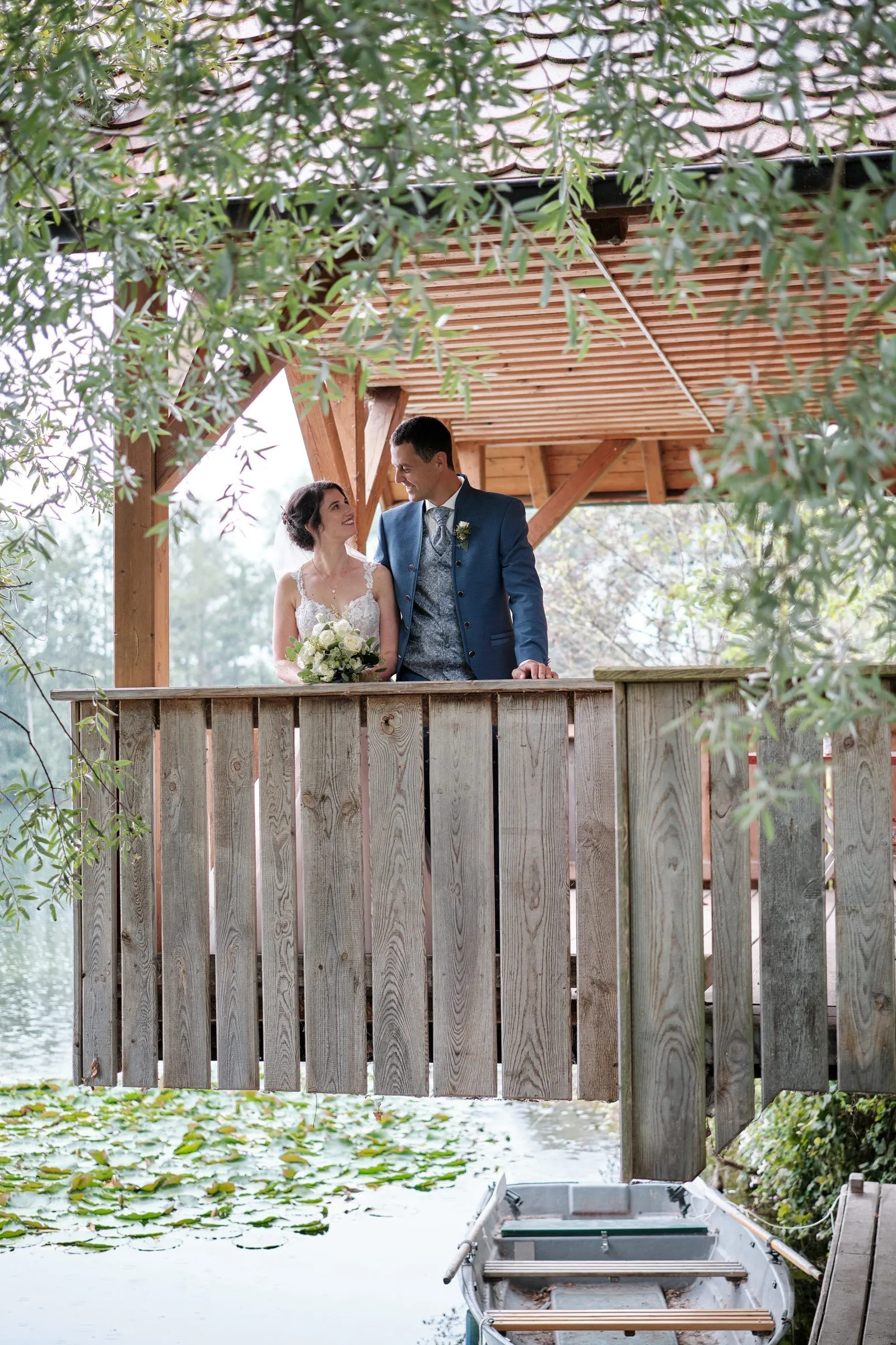 Brautpaar in einem Holzpavillon über dem Wasser, Ruderboot darunter – Hochzeit Christina & Manuel