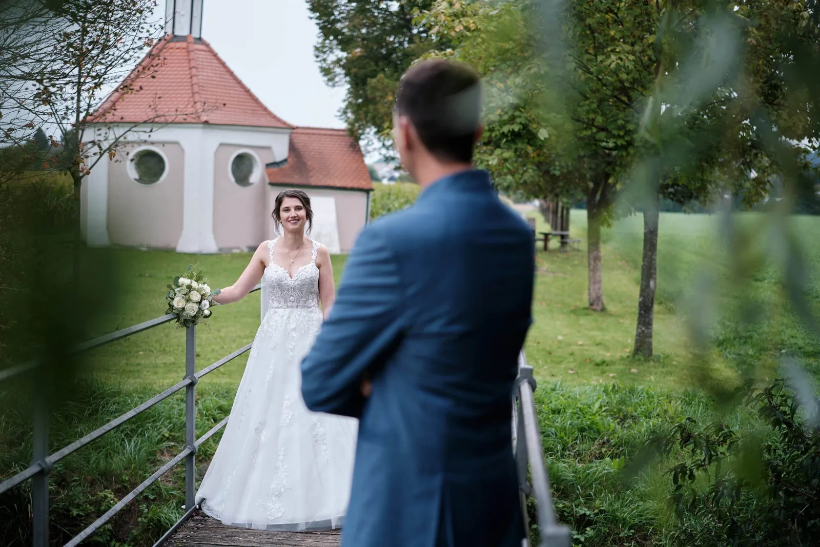 Braut auf einer Brücke, Bräutigam von hinten im Vordergrund – Hochzeit Christina & Manuel